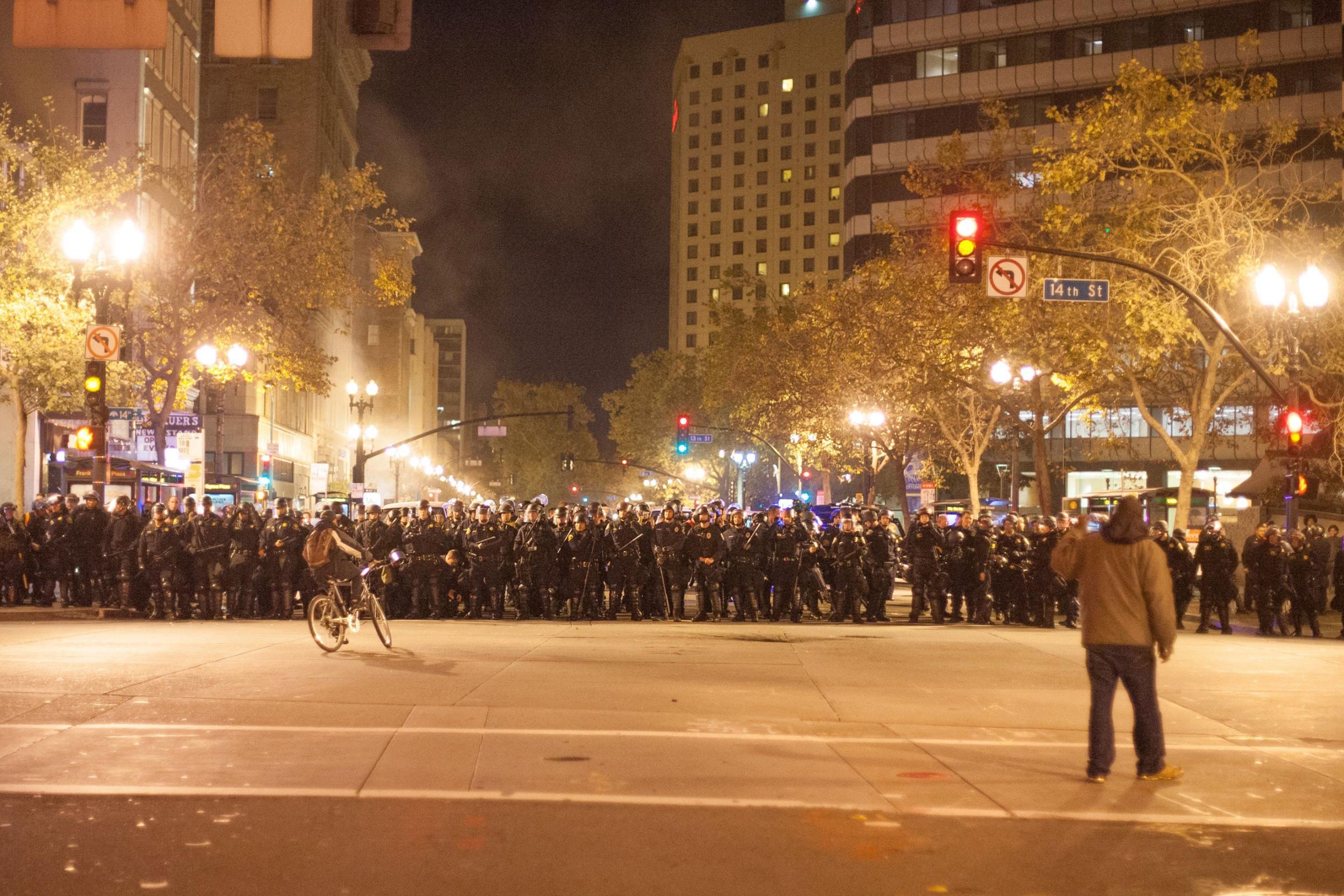A protestor on a bike rides in front of a crowd of police officers in full riot gear in Oakland, Calif., on Nov. 25, 2014.
