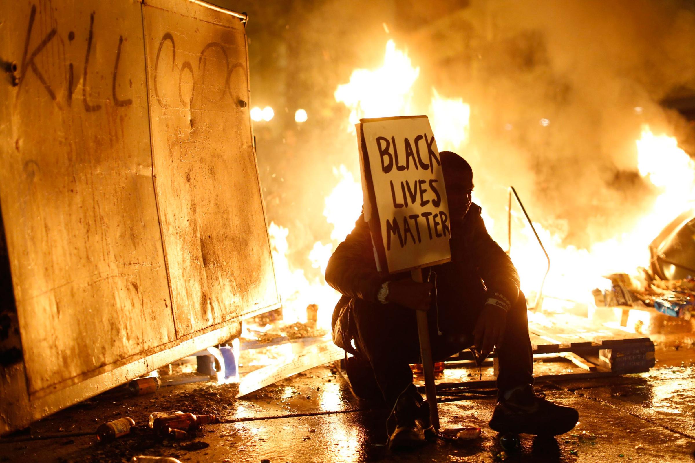 Flames burn behind a demonstrator in Oakland, Calif., on Nov. 25, 2014.