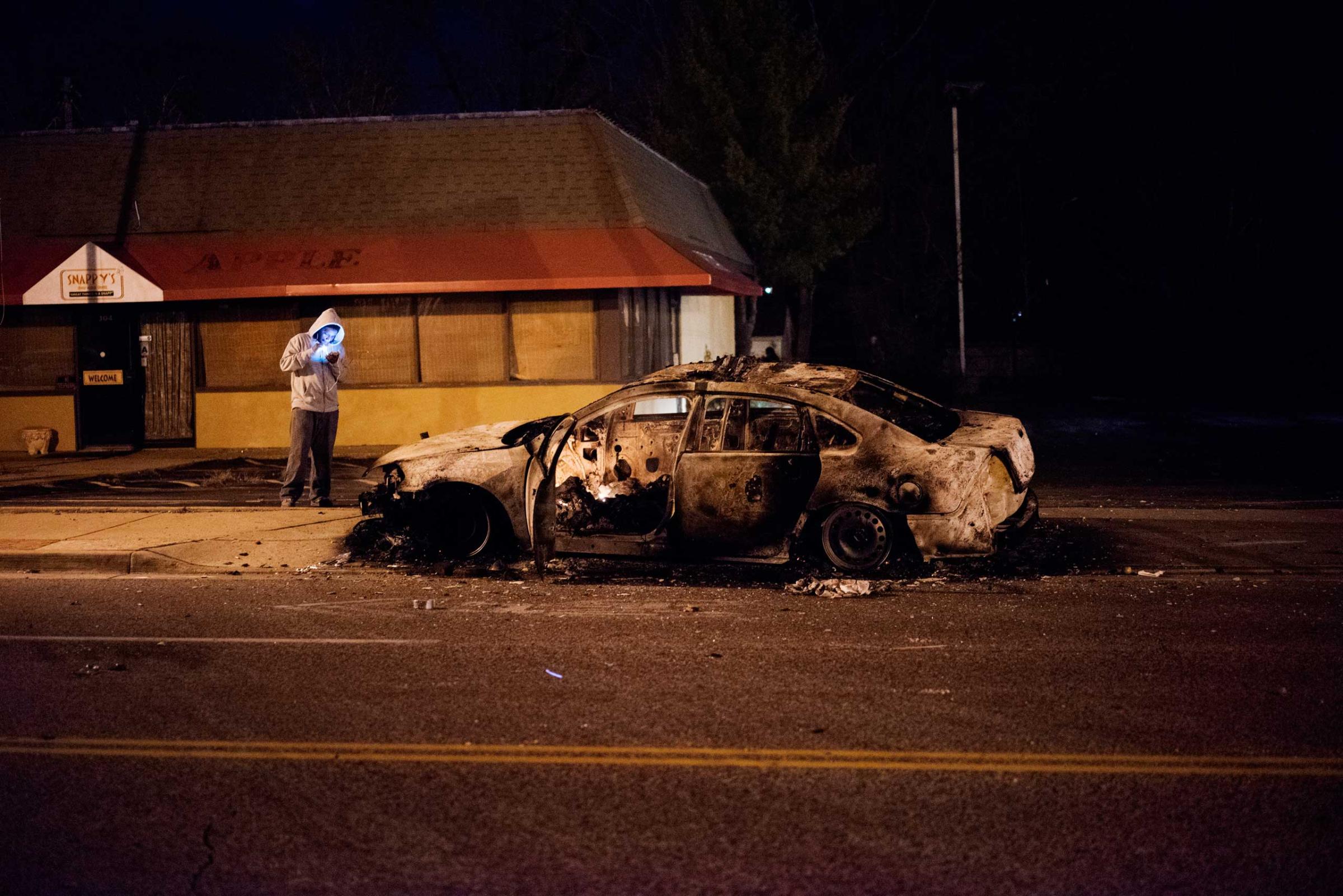A man stands by a burned out car in Ferguson, Mo. on Nov. 24, 2014