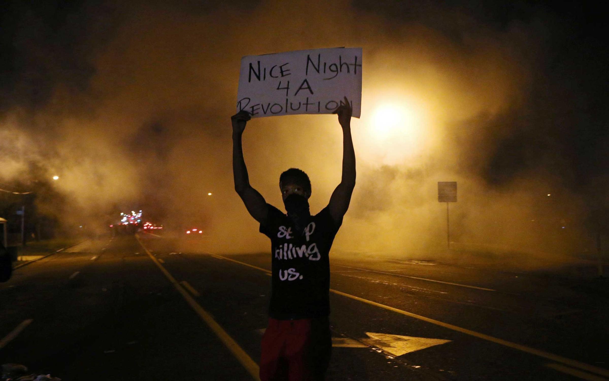 Aug. 17, 2014. A protester holds a sign towards the police after they shoot tear gas on W. Florissant in Ferguson. The protesters were throwing rocks and bottles towards the police.