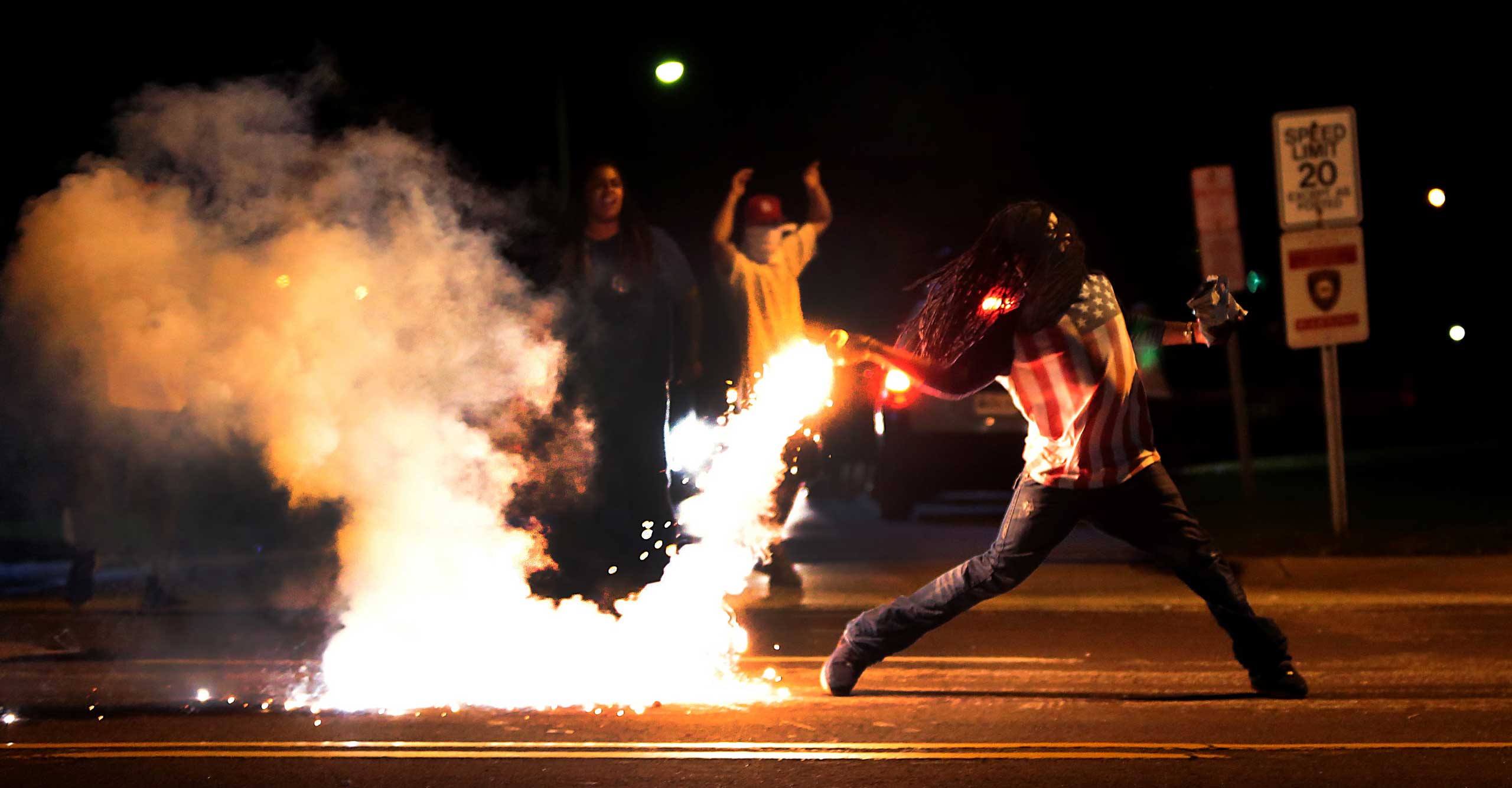 Aug. 13, 2014. A demonstrator throws back a tear gas container after tactical officers worked to break up a group of bystanders on Chambers Road and West Florissant on Wednesday, in St. Louis. Nights of unrest have vied with calls for calm in a St. Louis suburb where an unarmed black teenager was killed by police, while the community is still pressing for answers about the weekend shooting.