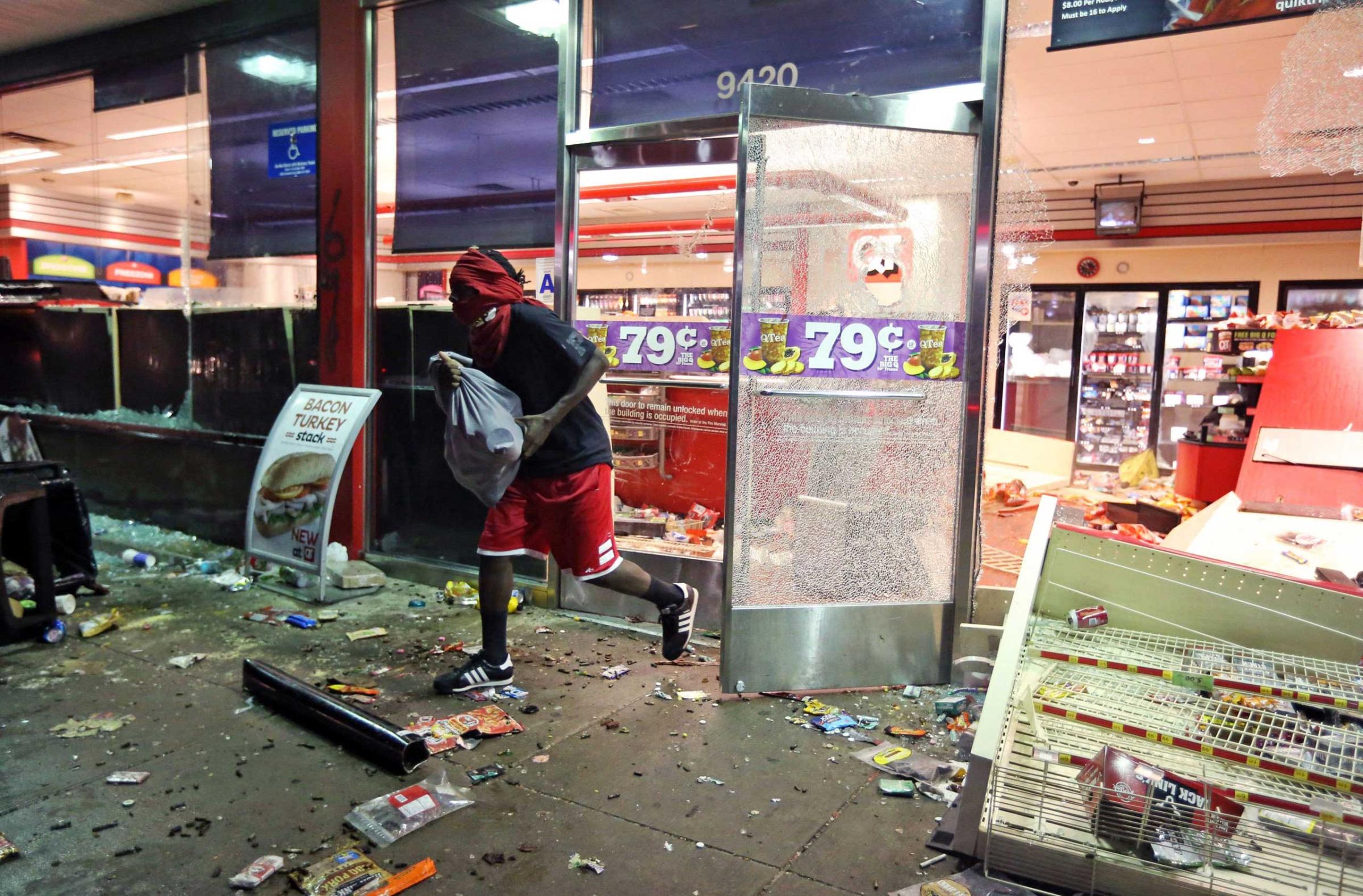 Aug. 10, 2014. A man leaves a store on Sunday, in Ferguson, Mo. A few thousand people crammed a suburban St. Louis street Sunday night at a vigil for unarmed 18-year-old Michael Brown who was shot and killed by a police officer, while afterward several car windows were smashed and stores were looted as people carried away armloads of goods as witnessed by an an Associated Press reporter.