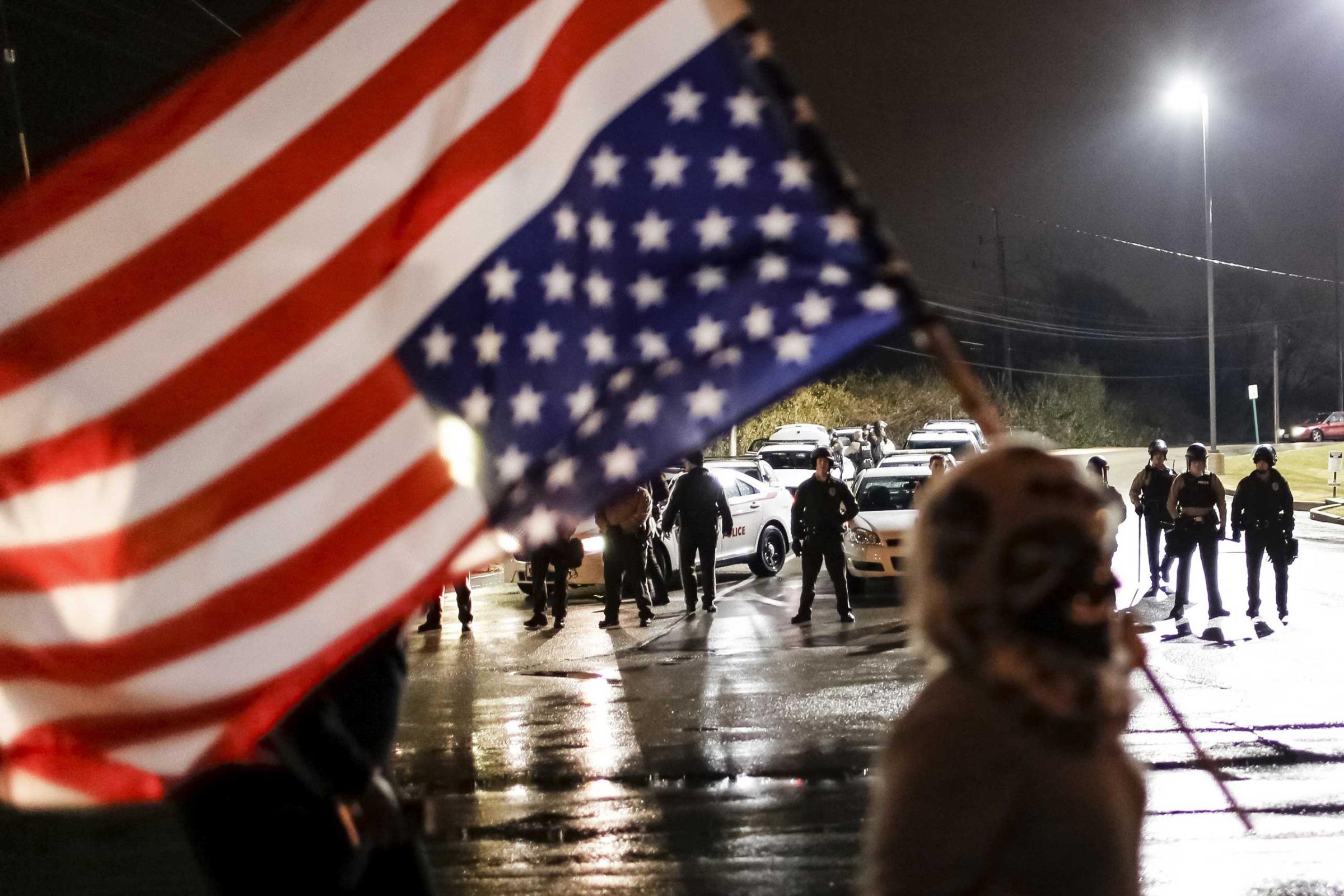 Police watch as a protester with an upside-down American flag marches along West Florissant Avenue in Ferguson, Mo.