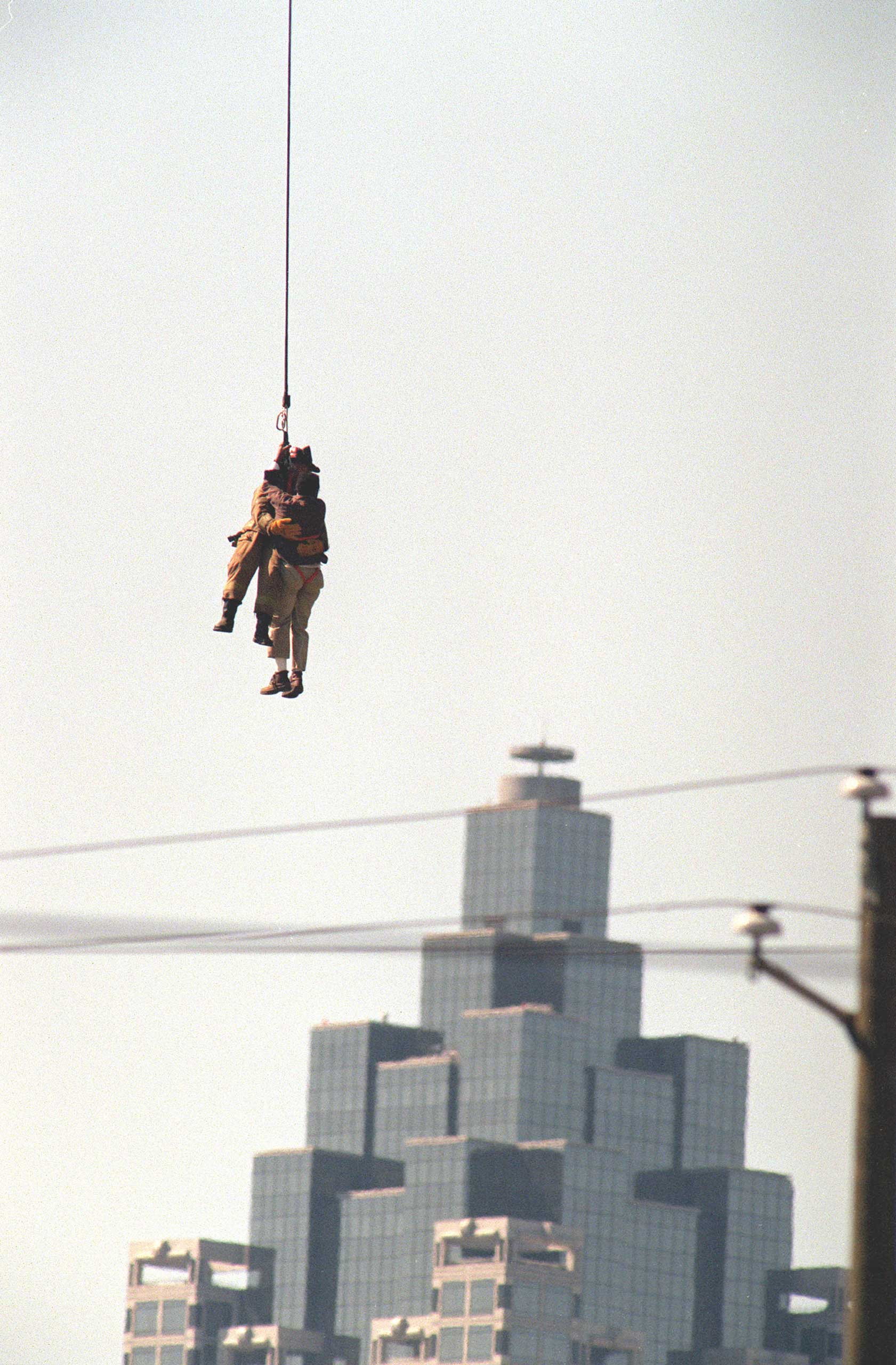 A firefighter dangles from a helicopter to rescue a stranded crane operator on April 12, 1999 in Atlanta.
