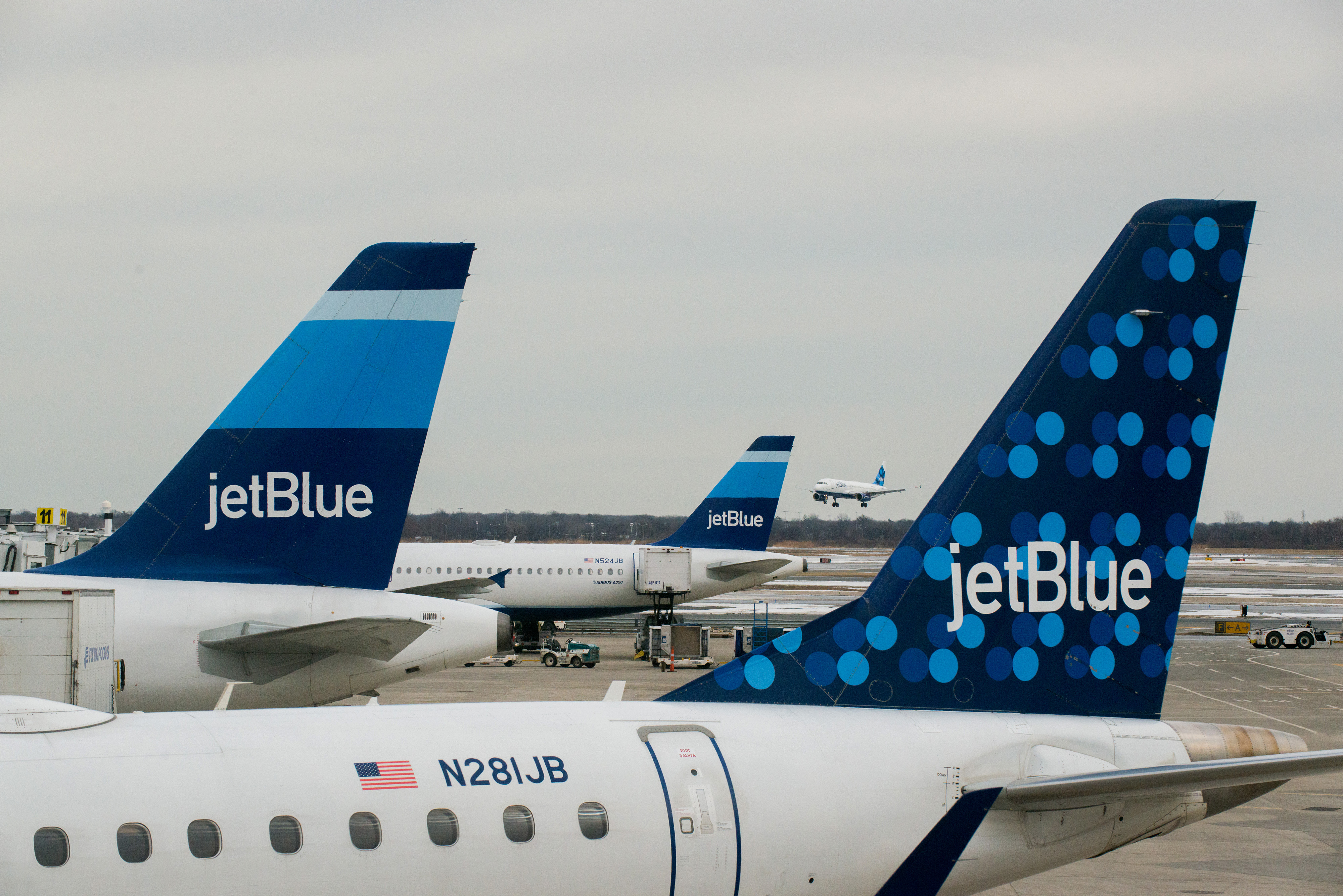 JetBlue Airways Corp. planes sit docked at the gates of Terminal 5 as another of the company's jets lands at John F. Kennedy International Airport in New York on Jan. 28, 2014.