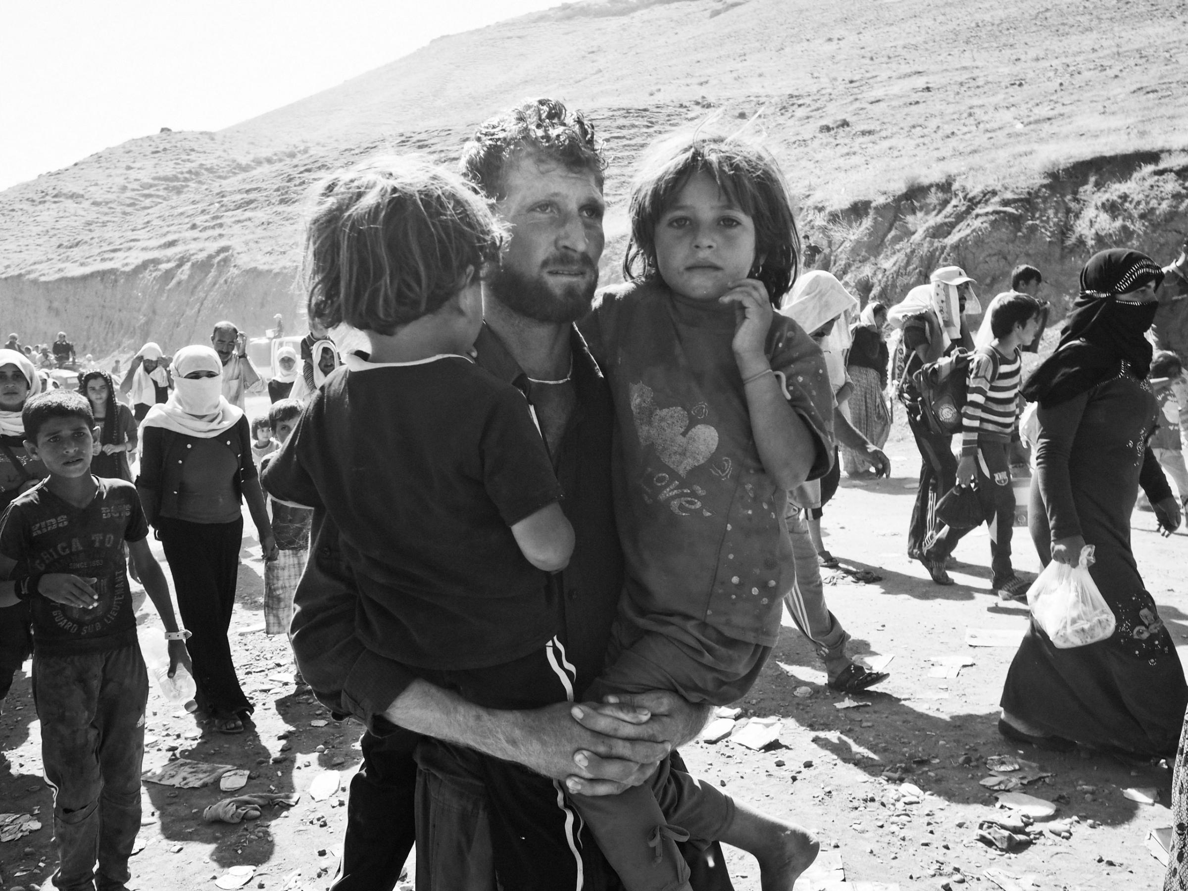 A displaced Yezidi man carries his two daughters as he crosses the border into Kurdish-controlled northern Iraq near the village of Fishkhabur. Iraq. Aug. 10, 2014.