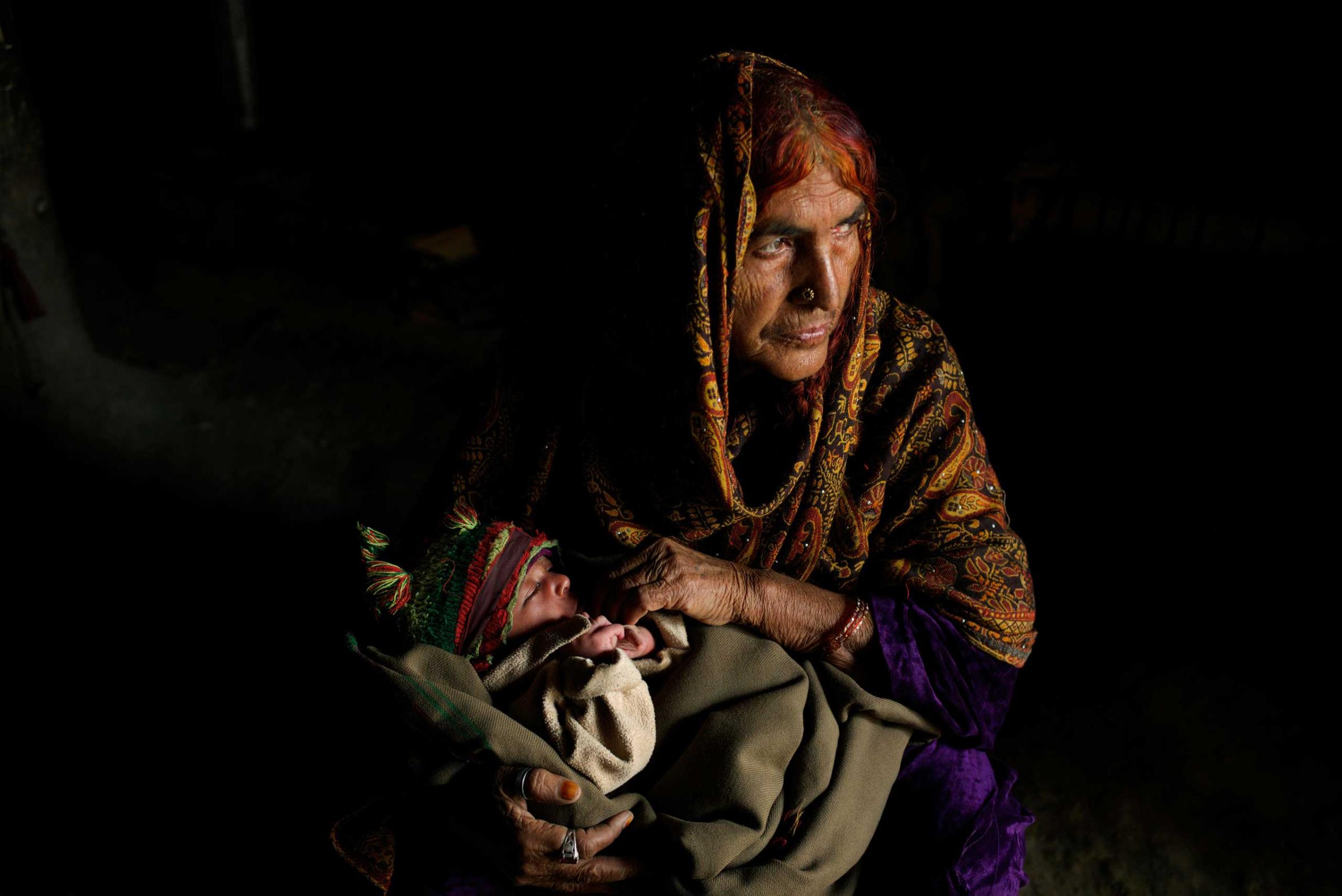 ISLAMABAD, PAKISTAN; FEBRUARY 2104 Holding her twenty-five day old grandson Ziaullah, elderly Bacha Hilal squats down in the mud hut that has become home since escaping conflict in Bajaur. “The first time the Taliban came our life became limited only to our house. They didn’t let us go to our fields or collect wood from the mountains and we weren’t even allowed to go to the river for water. They demanded that no child should go to school and anyone working for the government should abandon their jobs. They even banned dogs, cockerels and donkeys and instructed the men to start cultivating poppy. After Eid in 2008 the army came. They started shelling and their tanks began to flatten the houses… There was a big ditch in the land by our home and there were times we would spend two or three nights there taking shelter with the children. A lot of people were killed; the Taliban were slaughtering on the ground and the army was bombing from above. One day a mortar landed very close to us; the shrapnel hit my husband in the eye. At 4am the next morning we left. We were all so scared as there were landmines all around. Nobody stayed behind; our whole village fled”. Surrounded by a population from Pakistan’s tribal areas at a sprawling, illegal settlement near Islamabad, the sanctuary that Bacha Hilal found is one she fears will become her grave. “In Islamabad we live in poverty. We can’t even afford the smallest of things and don’t know if we will eat one day or the next. We’ve borrowed all we can against our lands but no longer have any money. We are still IDPs. Because of the fighting, we are in this condition”.