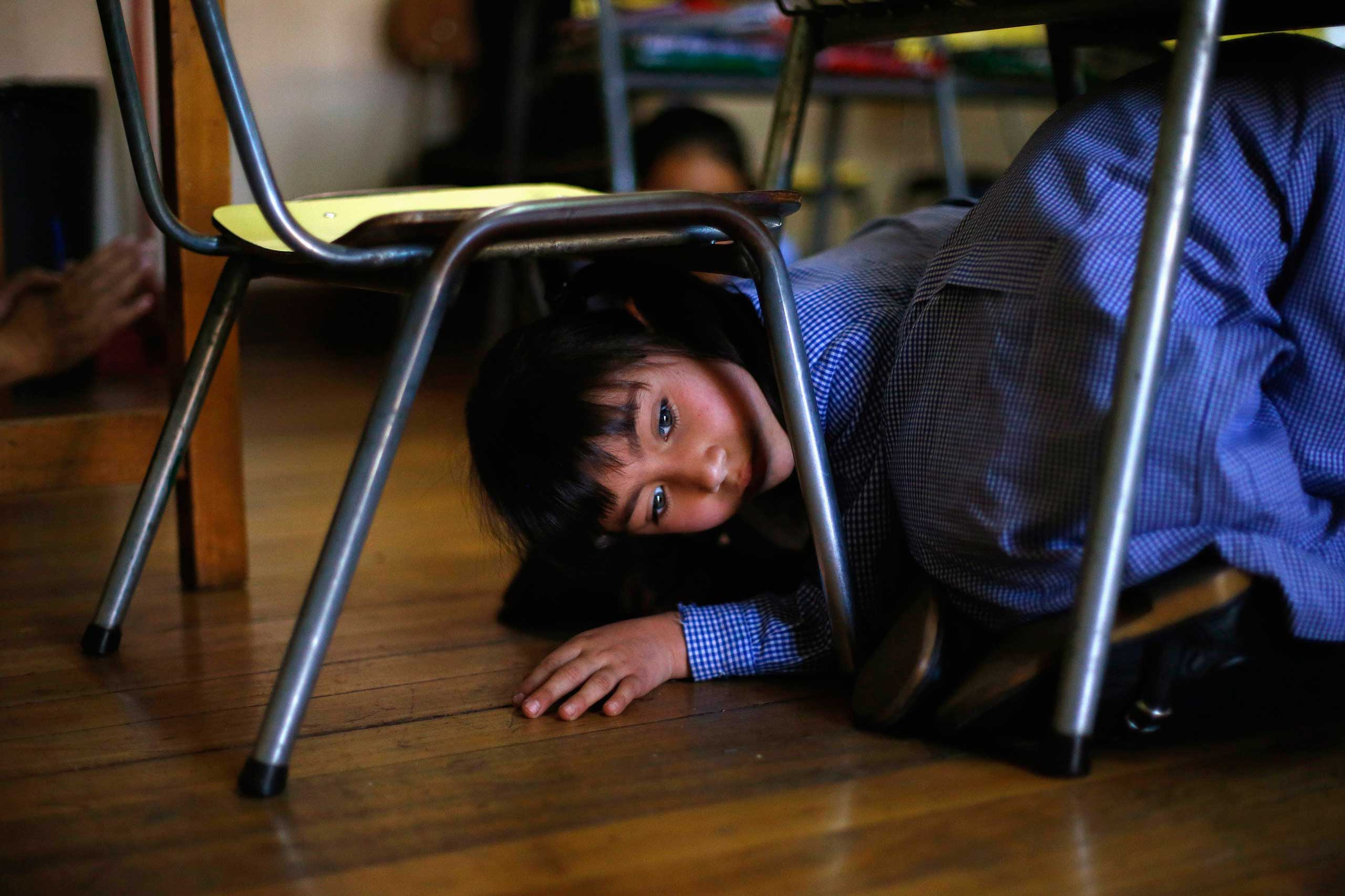 Nov. 13, 2014. A child takes cover under her school desks during an earthquake drill in Santiago.