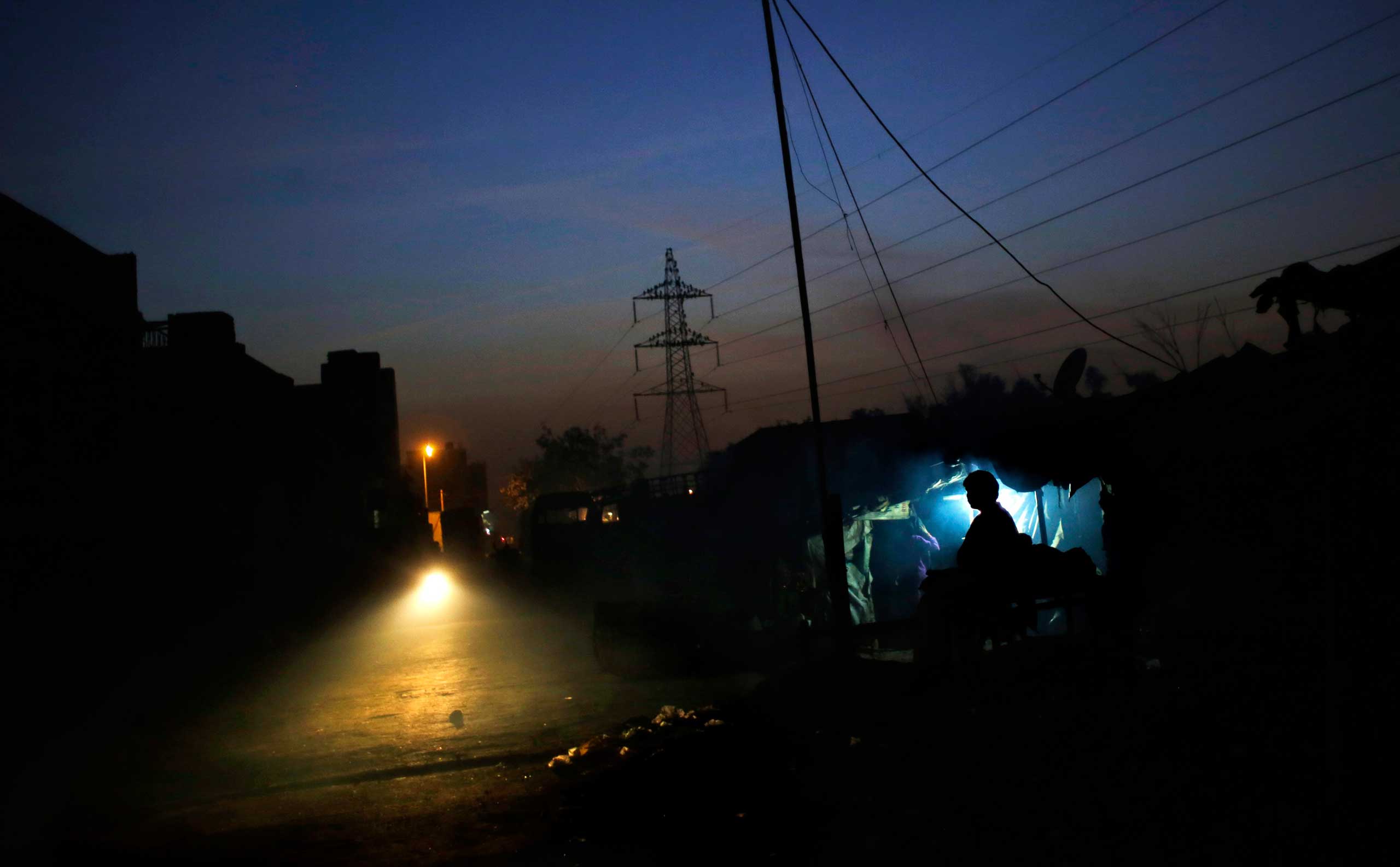 Nov. 13, 2014. An Indian man is silhouetted as he sits outside a roadside tea stall during a power outage on the outskirts of New Delhi. Long power cuts are common in rural and semi urban areas throughout India.