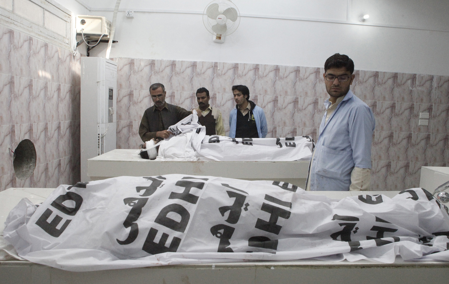 Hospital staff stand near the bodies of anti-polio drive campaign workers who were shot by gunmen, at a hospital morgue in Quetta