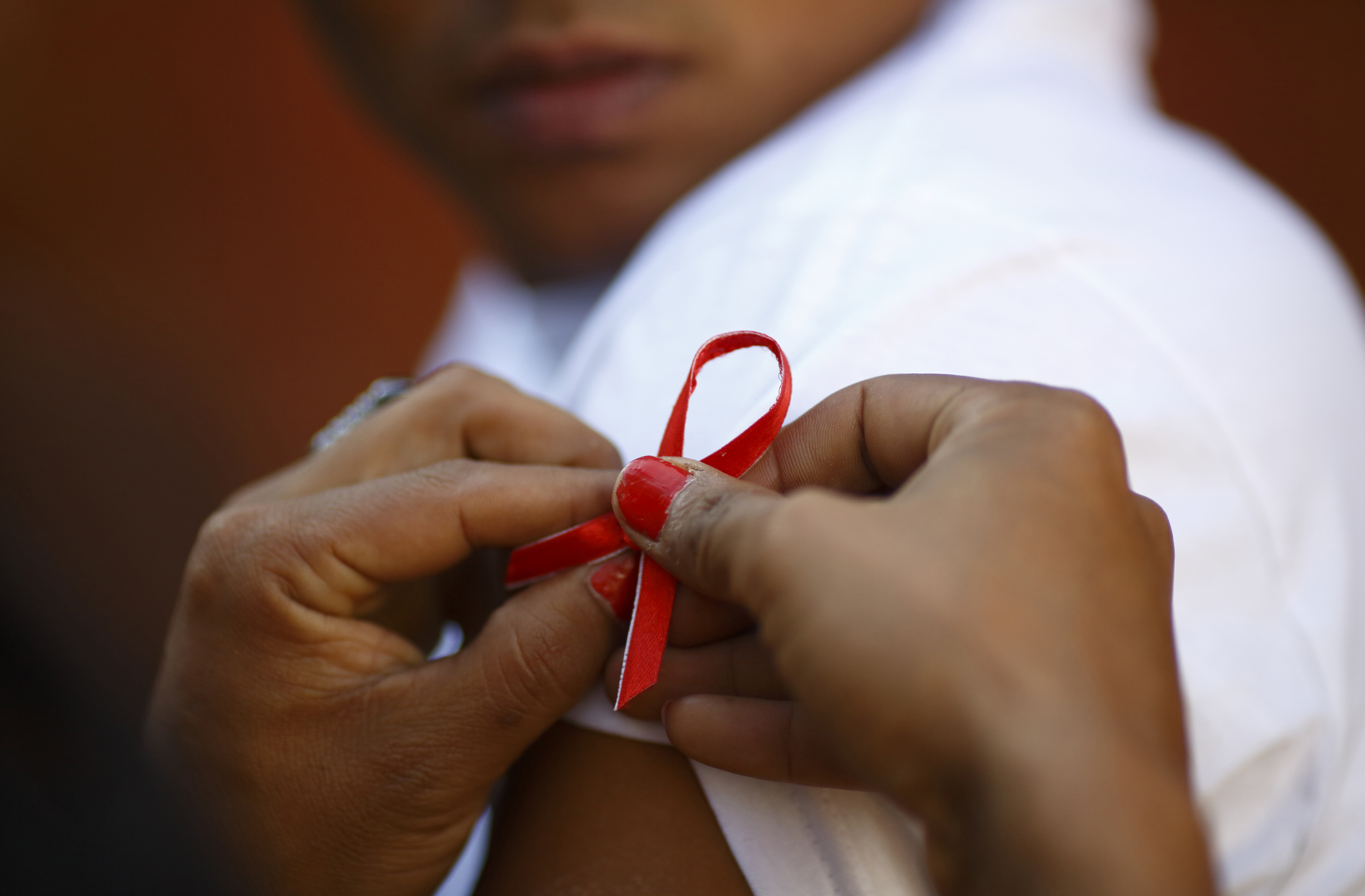 A red ribbon is put on the sleeves of a man by his friend to show support for people living with HIV during a program to raise awareness about AIDS on World AIDS Day in Kathmandu