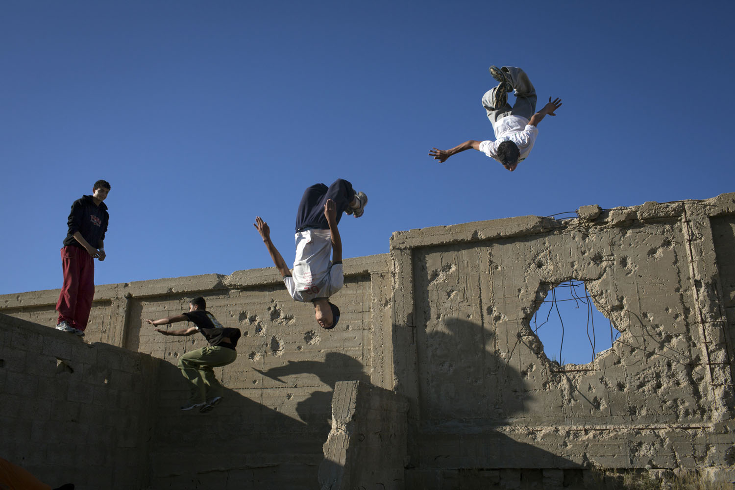 The Gaza Parkour team practices in a cemetery  on the outskirts of their refugee camp in Khan Younis, Gaza. The walls show damage from past Israeli incursions.