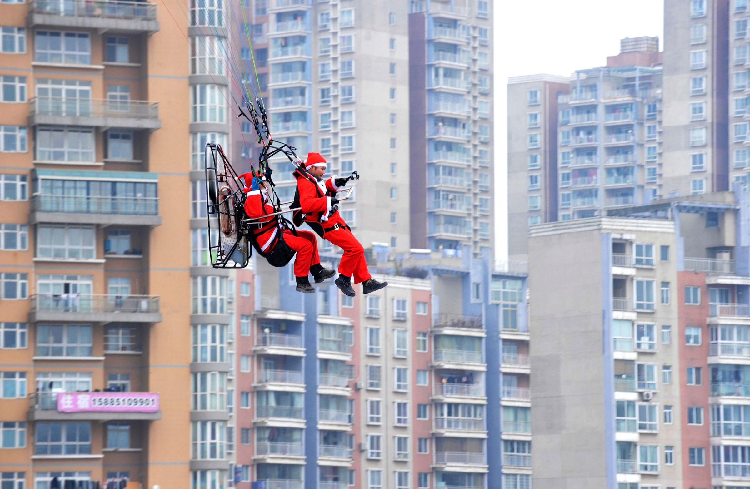 Members of a local powered parachute club wearing Santa Claus costumes fly past residential buildings to drop presents to pedestrians during a promotional event celebrating Christmas in Guiyang, Guizhou province on Dec. 24, 2014.