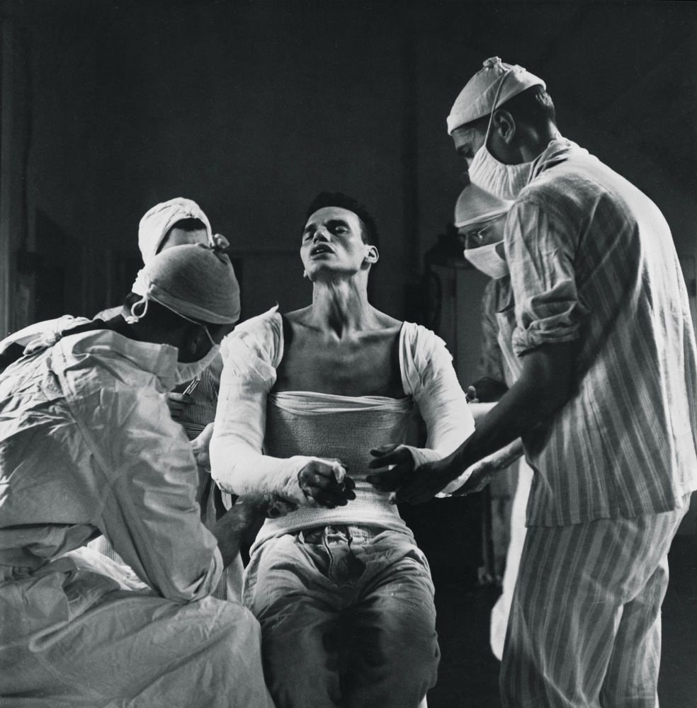 George Lott, 22, a medic attached to a battalion aid station of the 137th Infantry Regiment in Patton’s Third Army, was wounded in both arms by German mortar fire in France in 1944. Here, he suffers as doctors mold a plaster cast to his body.