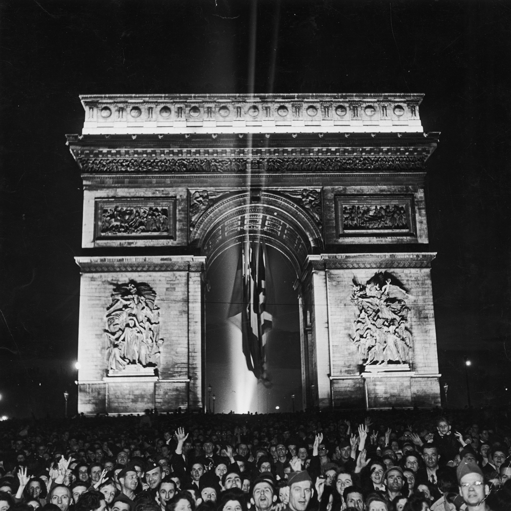 Night view of a crowd of jubilant civilians and troops celebrating the end of the war in Europe, Paris, May 1945.