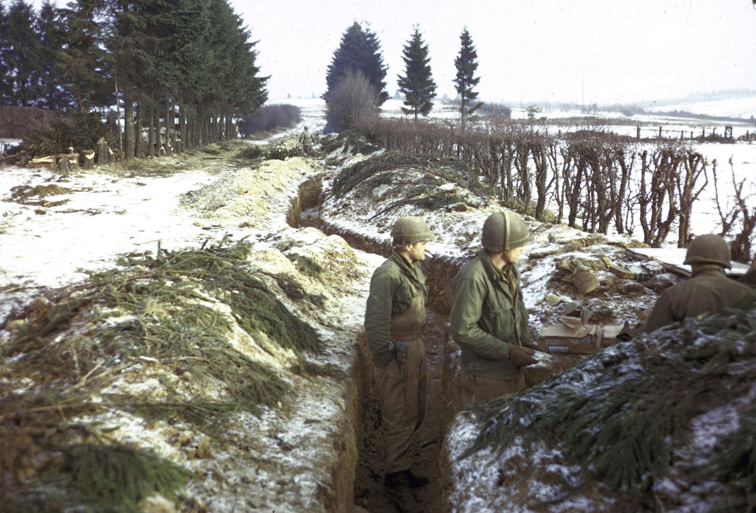 American troops man trenches along a snowy hedgerow in the northern Ardennes Forest during the Battle of the Bulge.
