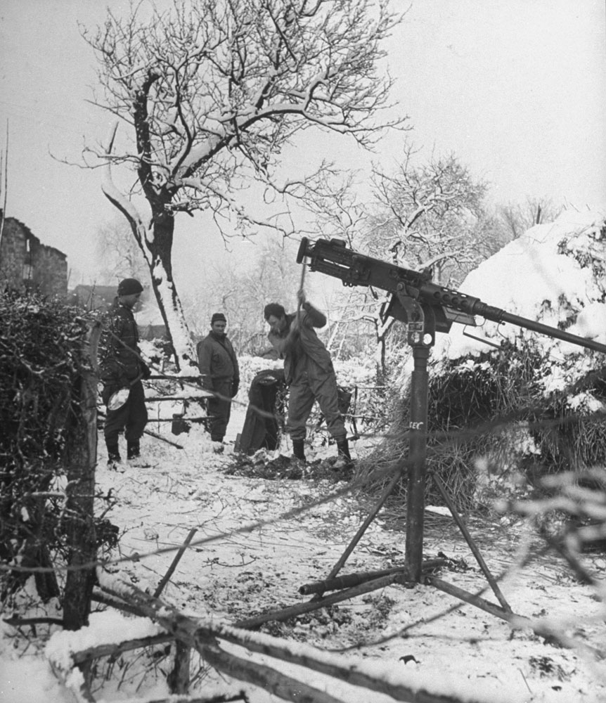 American GI's chop a foxhole in the frozen ground by a haystack during the Battle of the Bulge. The machine gun was set up in preparation for a German counterattack, expected at any moment.