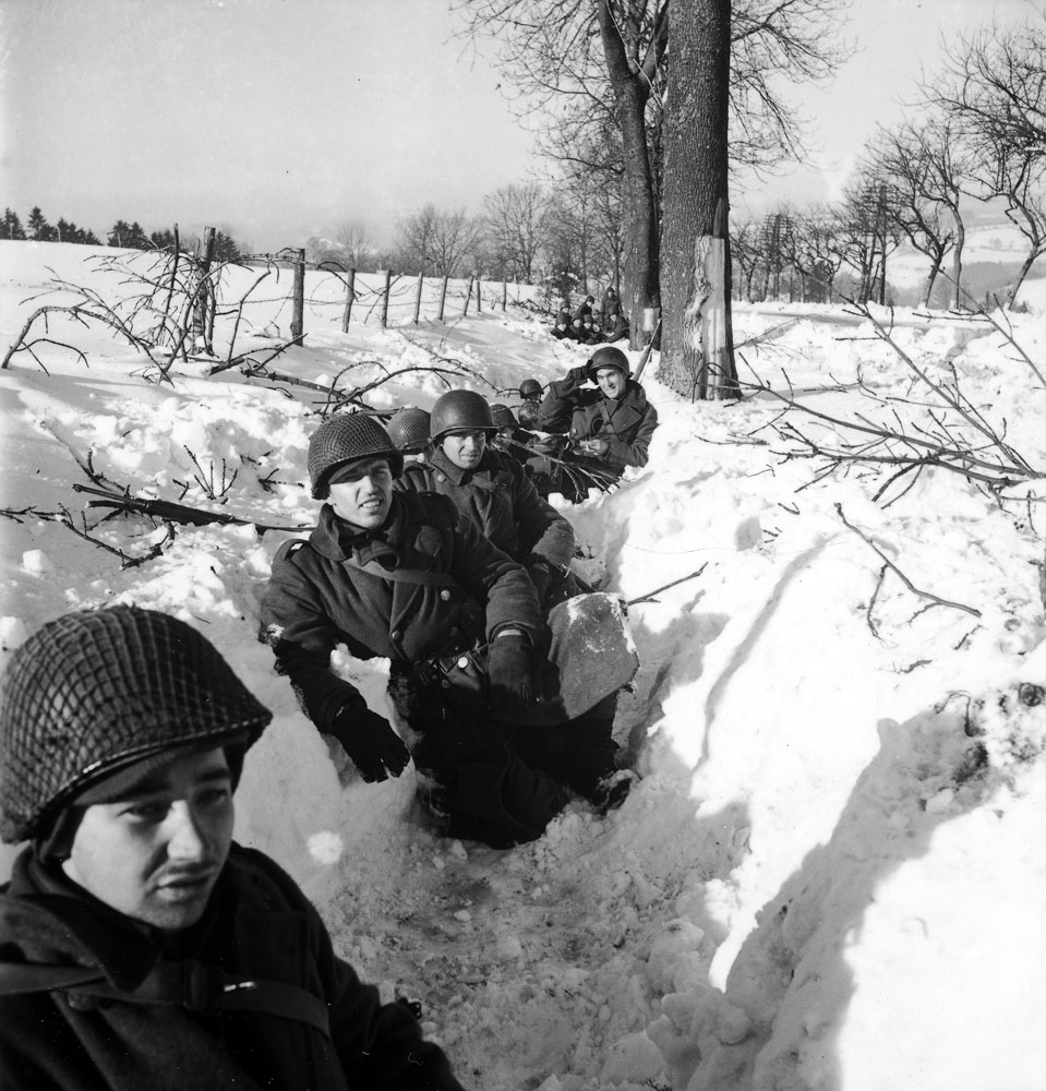 American troops in a snow-filled trench during the Battle of the Bulge.