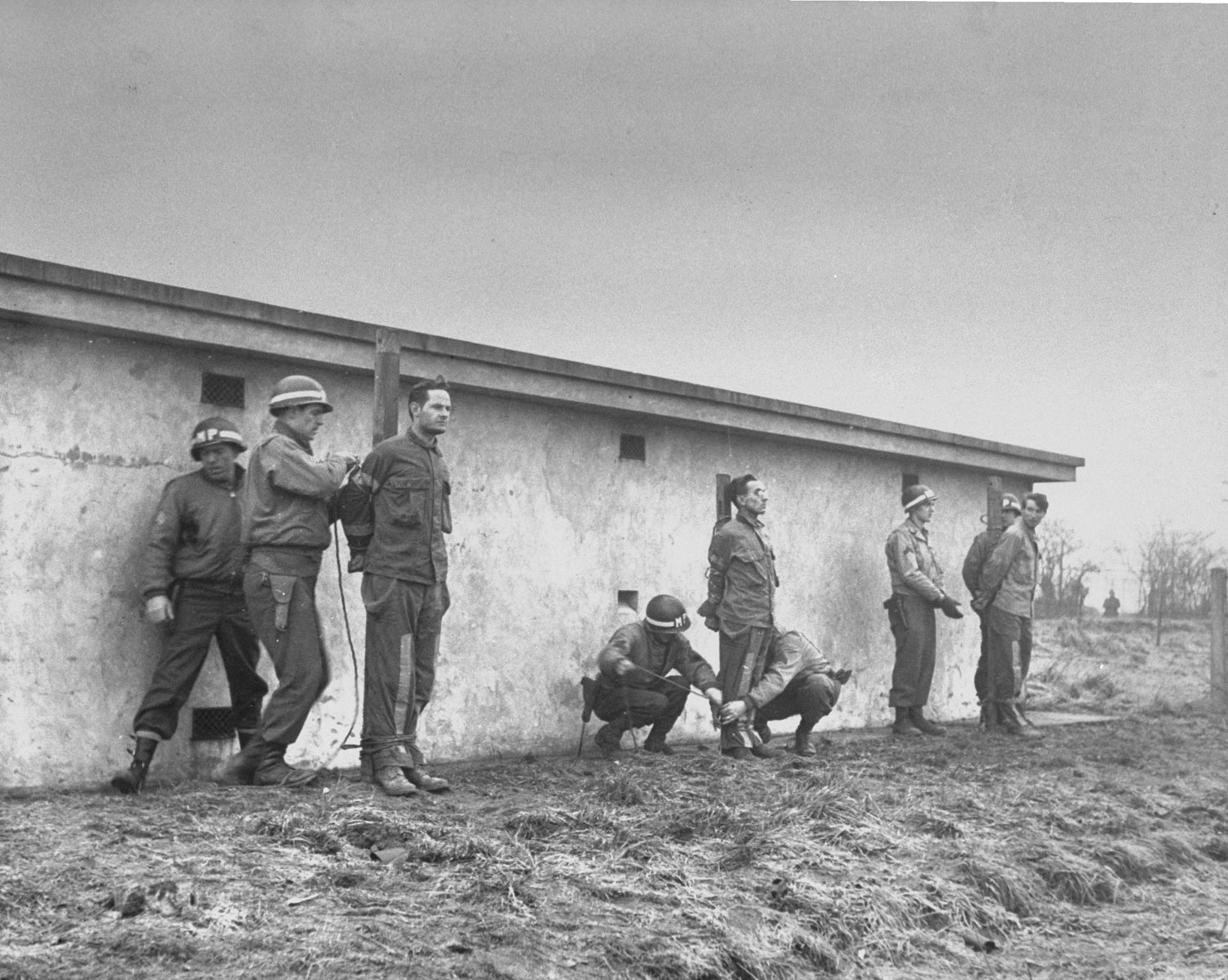 Photographed on Dec. 23, 1944, but not published in LIFE until June 1945. Behind a cell block, German prisoners are bound to stakes by MPs. Tried and convicted as spies, they are about to be executed.