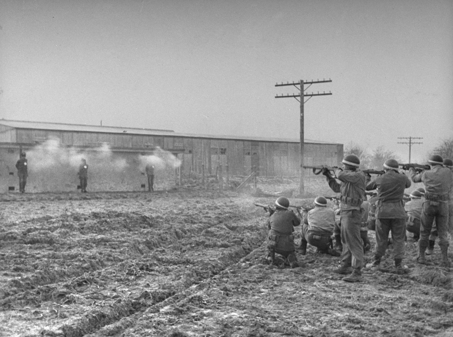 The volley is fired and three white puffs of smoke appear against the wall of the concrete block. The initial burst killed all three almost instantaneously. The firing squad, all military police, consisted of three groups of eight men, each with one additional marksman along as a spare.
