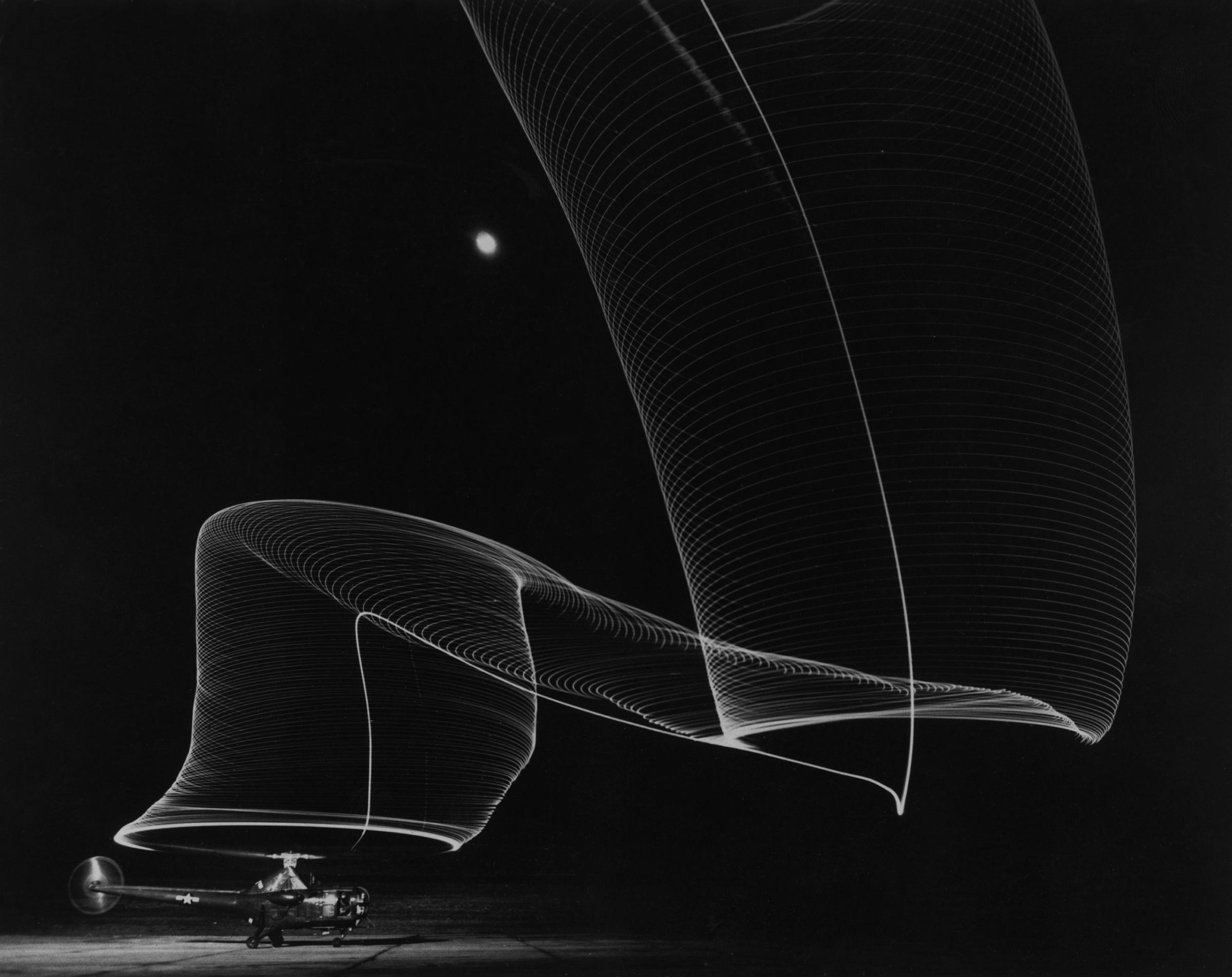 Slinky-like light pattern produced by light-tipped rotor blades of a helicopter as it takes off into the dark sky, 1949.