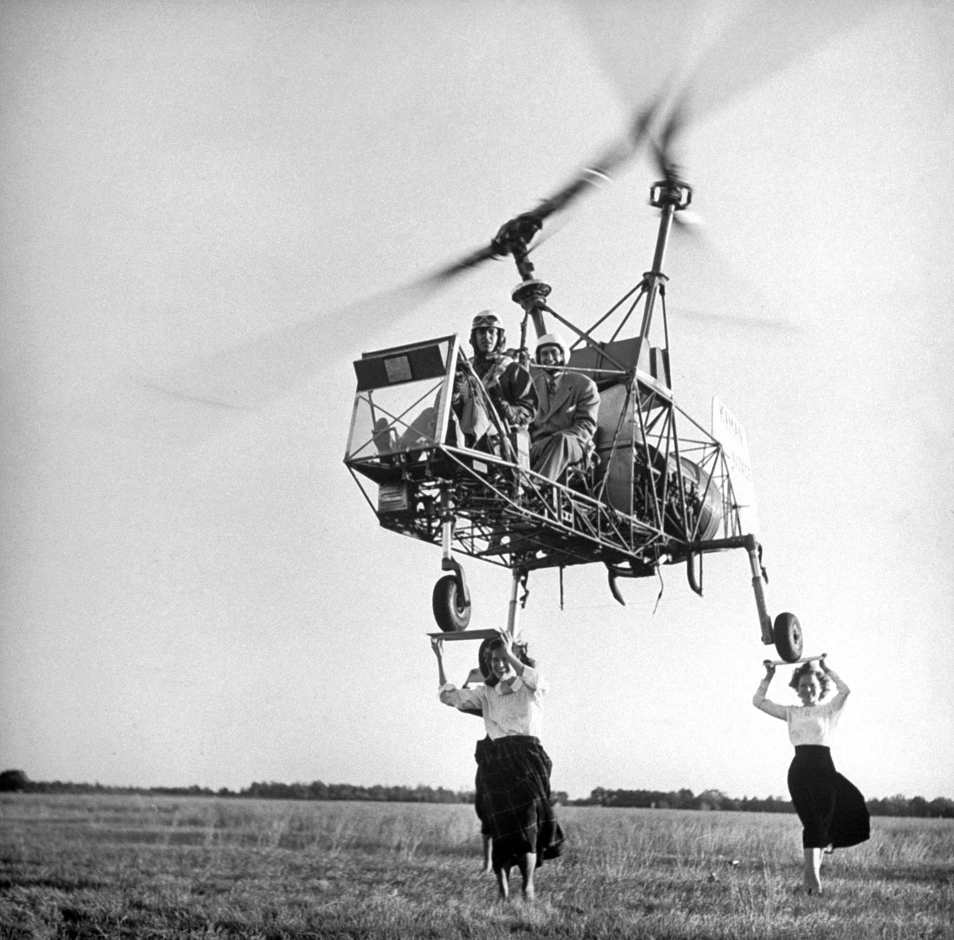 A "K190" helicopter attempting a three-point landing atop the heads of three women holding plywood squares as landing "pads," 1948.
