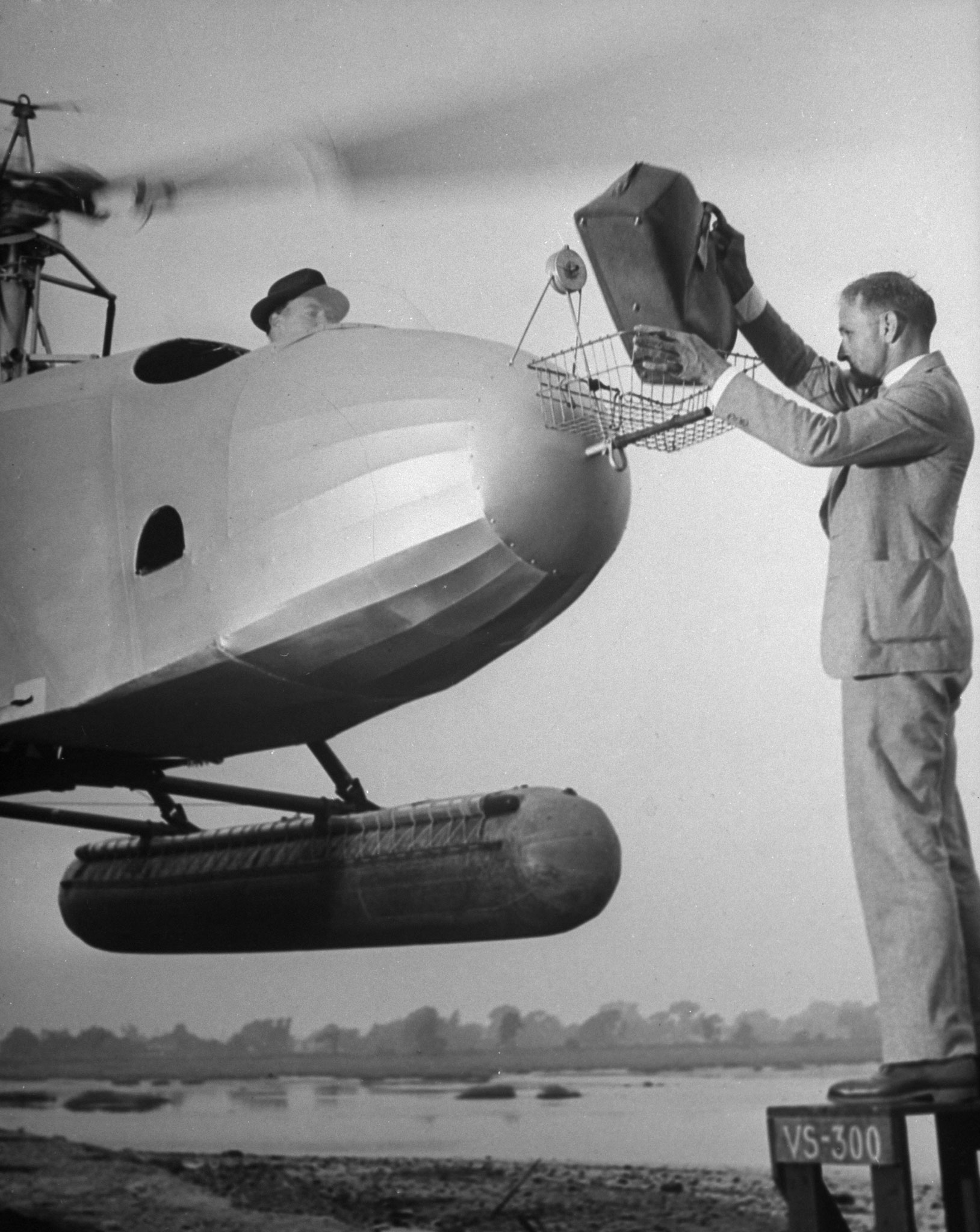 A man drops a briefcase into the basket on the nose of a helicopter, 1942.
