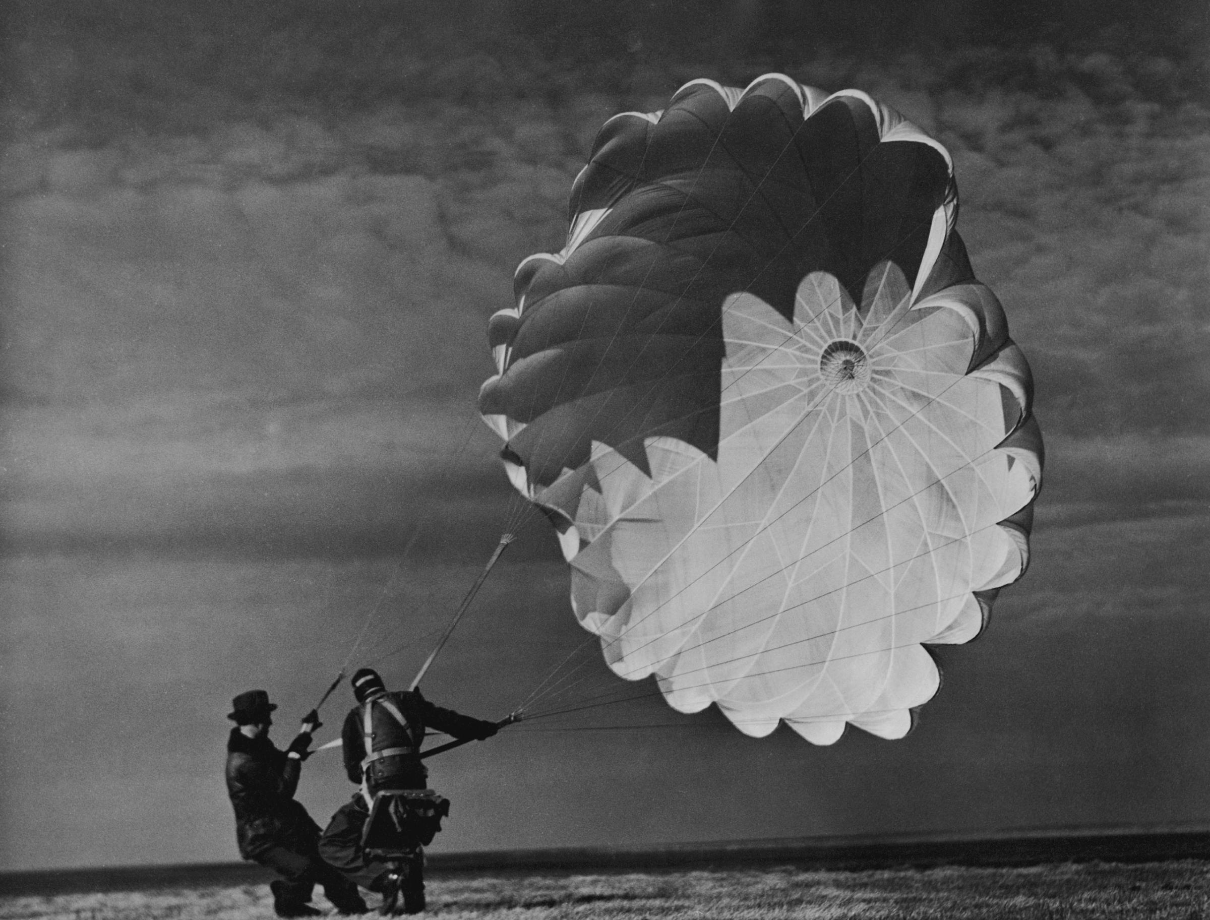 A parachute jumper testing equipment for the Irving Air Chute Co. gets some help while struggling to reel in his billowing chute, 1937.