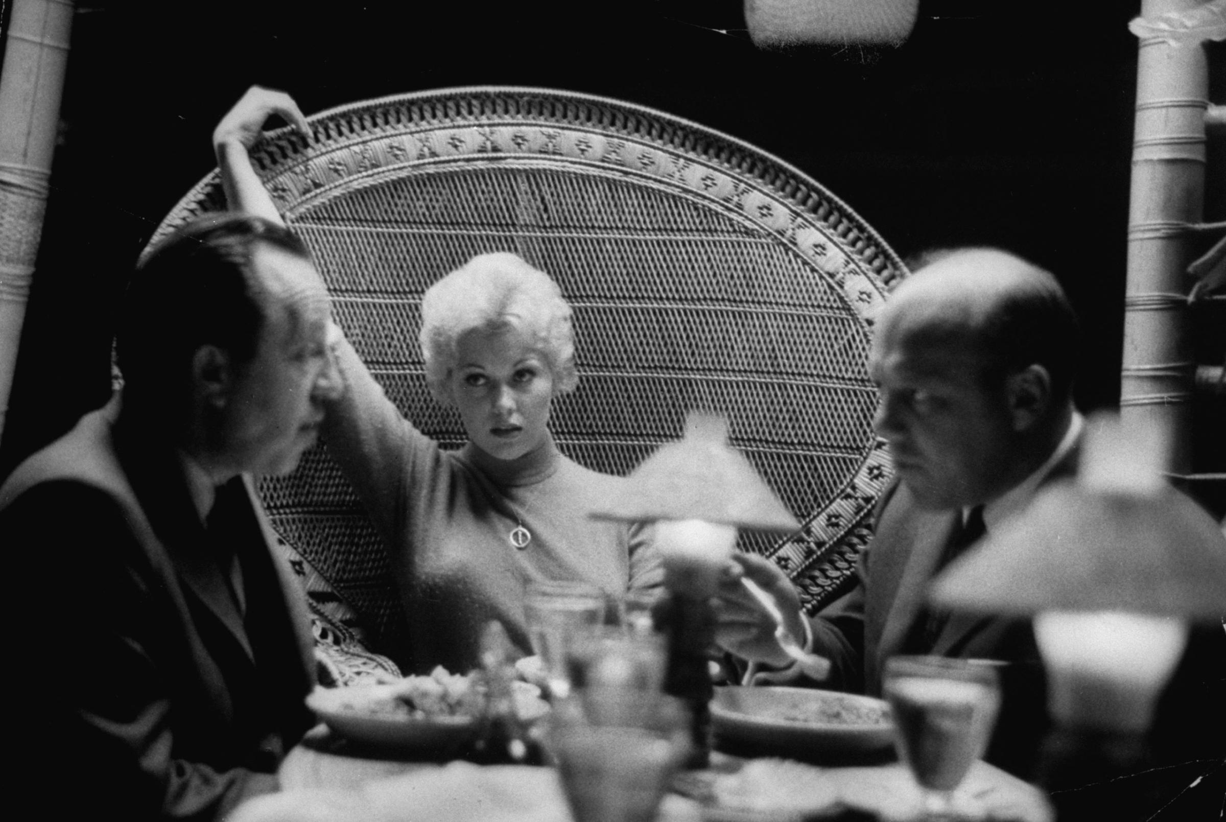 In a Beverly Hills Restaurant Kim Novak sits with a faraway look as agents Al and Wilt Melnick hotly discuss her blossoming movie career.
