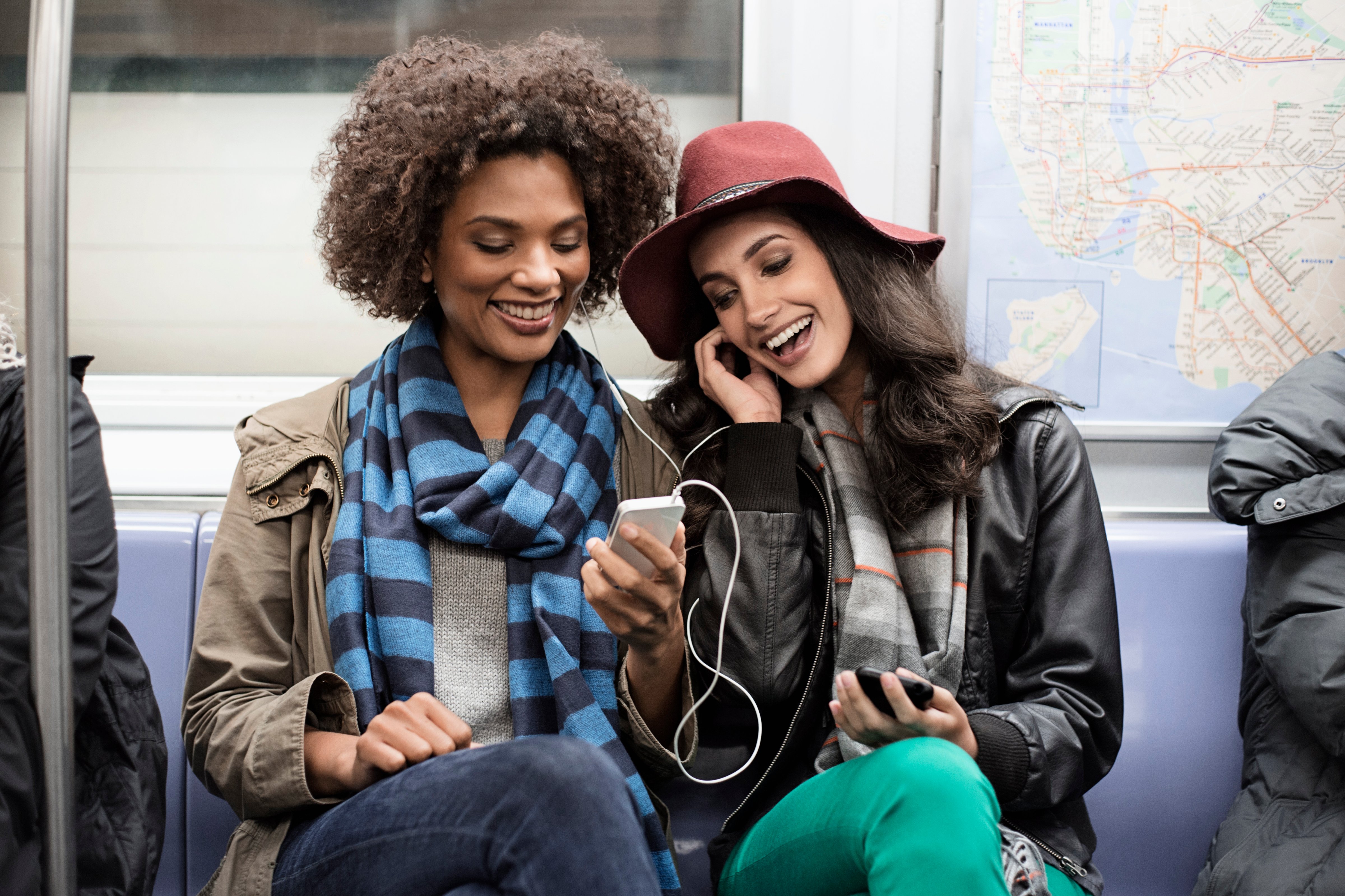 Women sharing earphones on subway (Image Source RF/DreamPictures&mdash;Getty Images/Image Source)