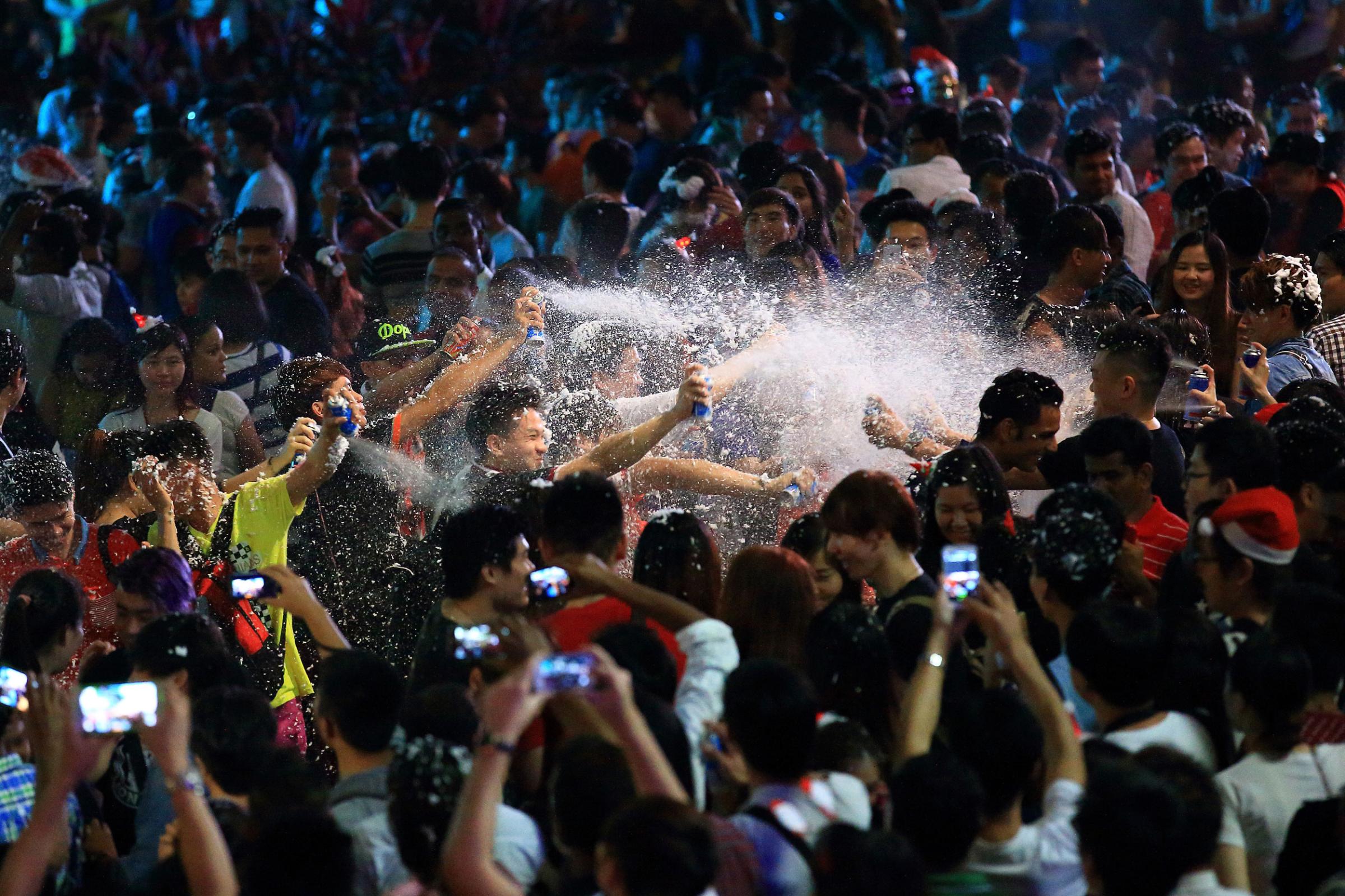 People release snow spray at each other to usher in Christmas along Orchard Road on December 25, 2014 in Singapore.