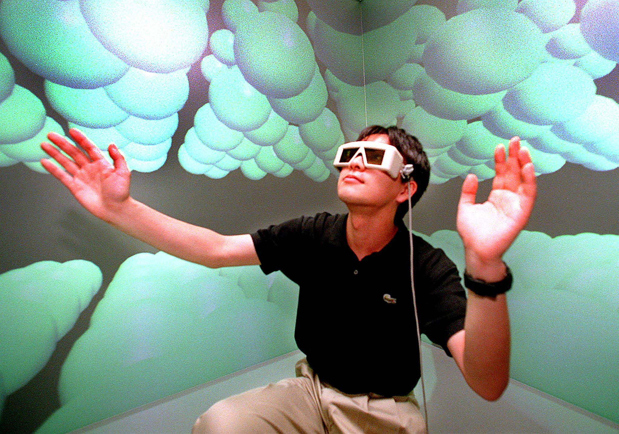 A researcher at Tokyo University's Intelligent Modeling Laboratory wearing 3-D glasses, extending his hands to touch carbon atoms in the microscopic world at the laboratory's virtual reality room.