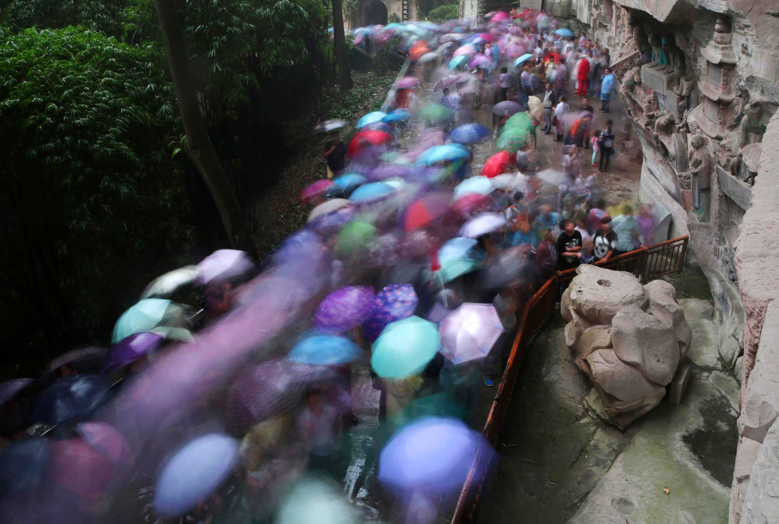Tourists holding umbrellas crowd visit the stone sculptures at the Baoding Mountain on the third day of the seven-day national day holiday, in Chongqing municipality, Oct. 3, 2014.