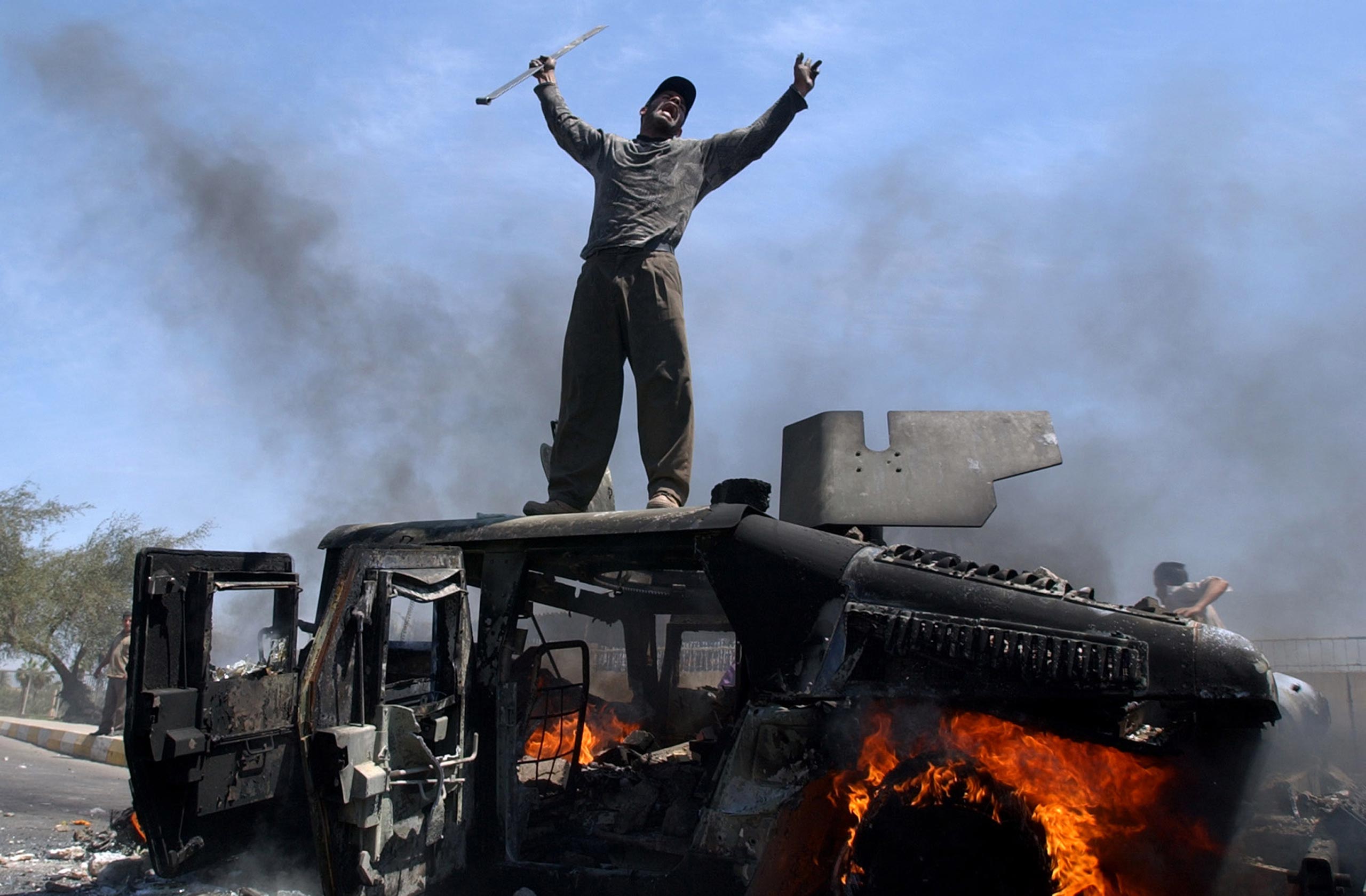An Iraqi man celebrates atop of a burning U.S. Army Humvee in the northern part of Baghdad on April 26, 2004.