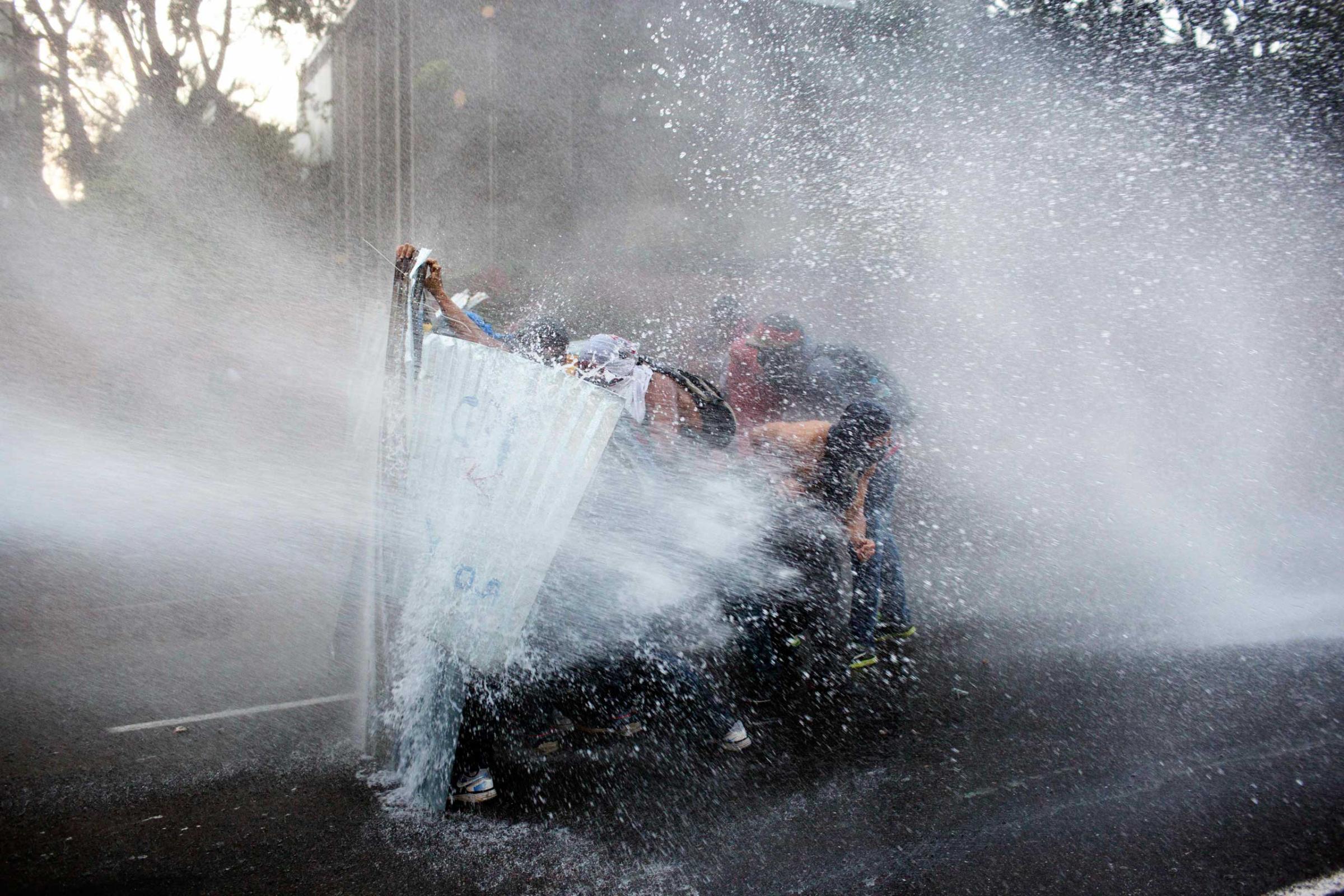 Anti-government demonstrators take cover from a police water cannon in Caracas, Venezuela, Feb. 28, 2014.