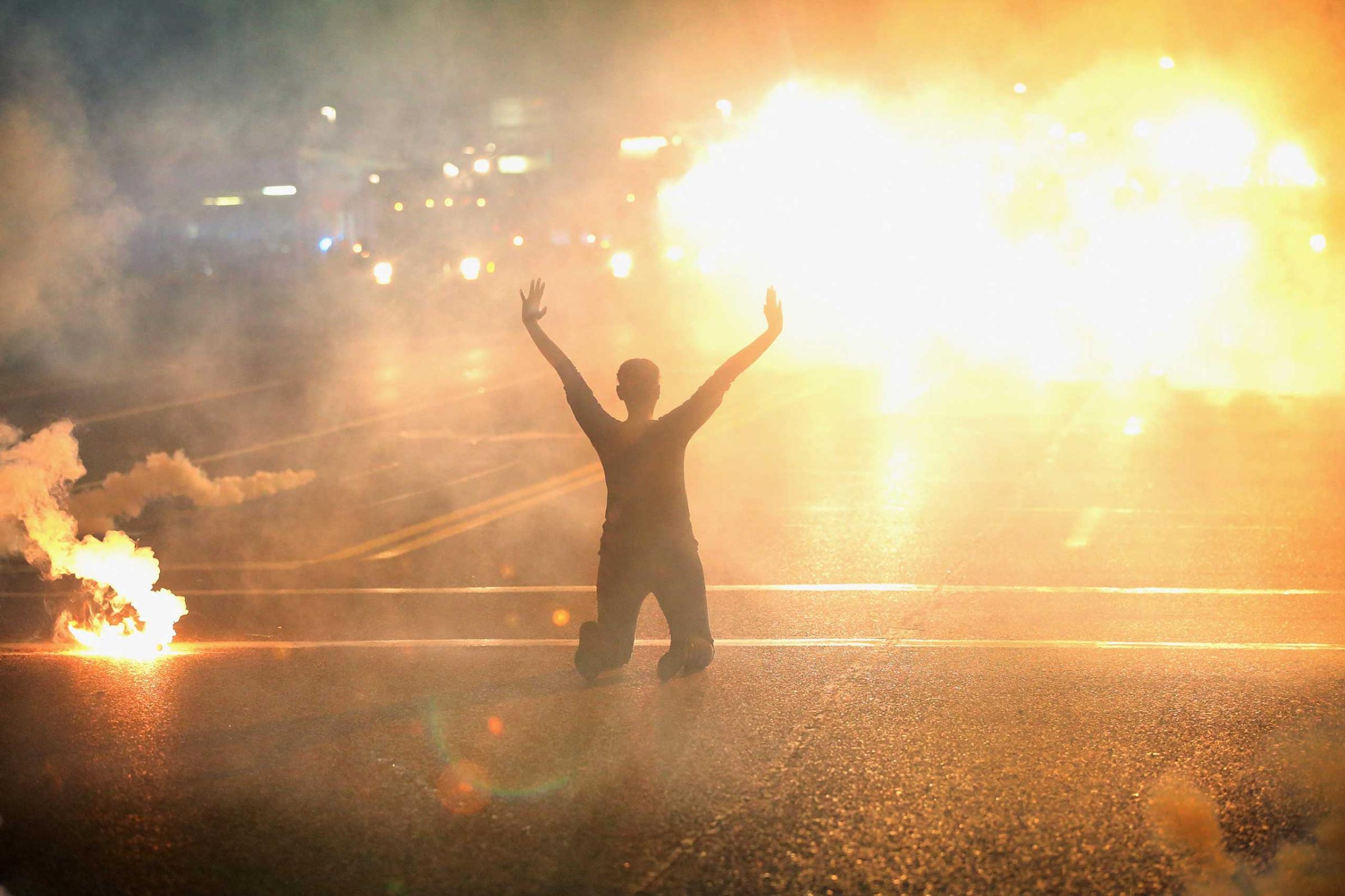 Tear gas reigns down on a woman kneeling in the street with her hands in the air after a demonstration over the killing of teenager Michael Brown by a Ferguson police officer on Aug. 17, 2014 in Ferguson.