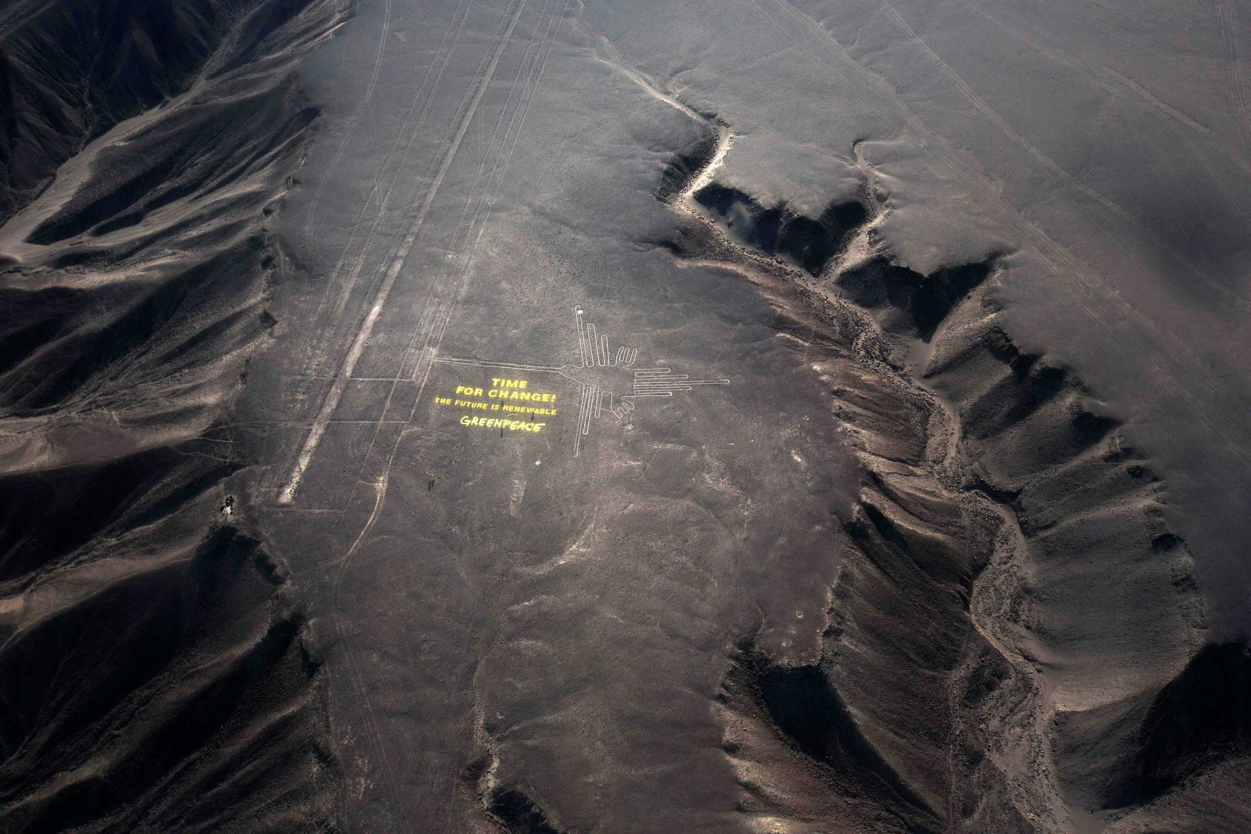 Greenpeace activists stand next to massive letters delivering the message "Time for Change: The Future is Renewable," next to the hummingbird geoglyph in Nazca in Peru,, Dec. 8, 2014. (Rodrigo Abd—AP)