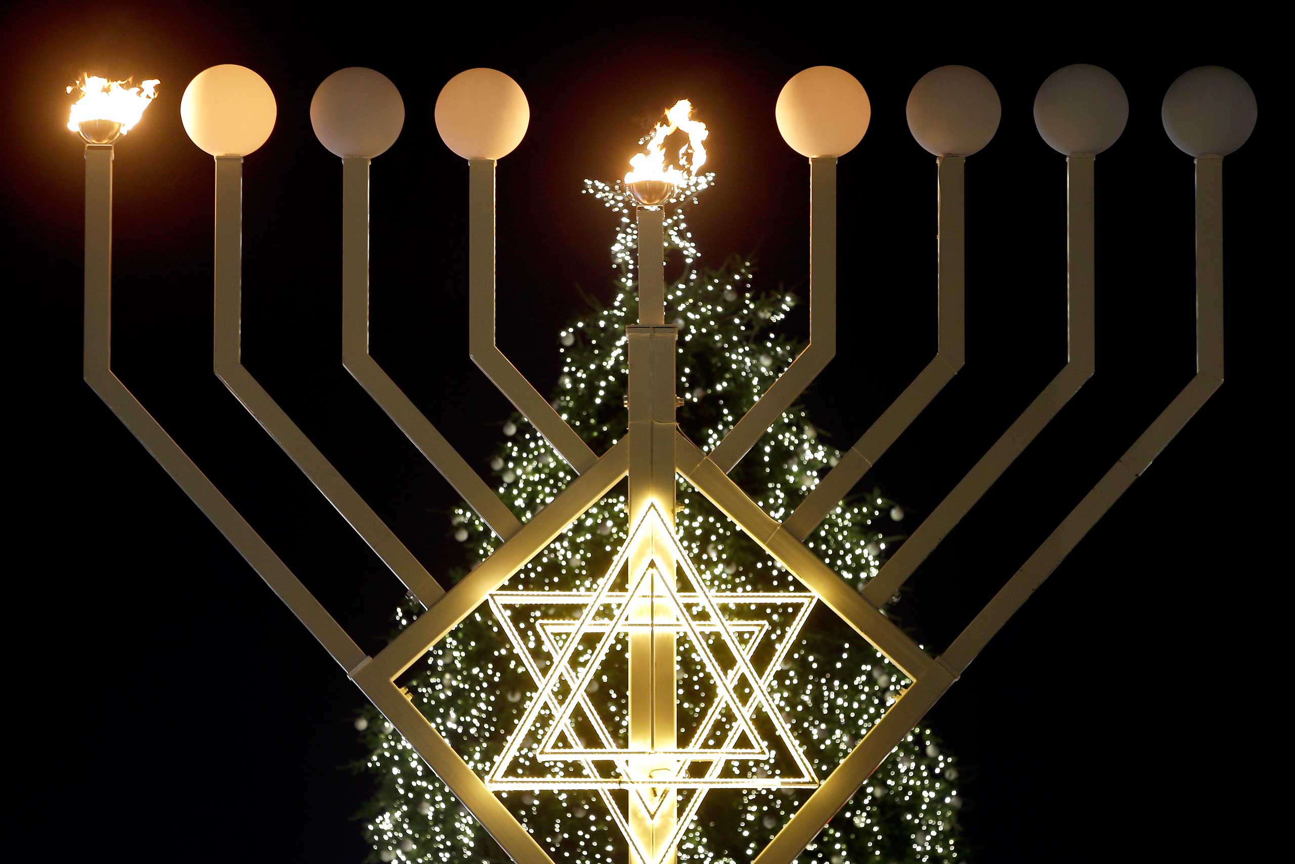 The first flames of a giant Hanukkah Menorah in front of a Christmas tree at the Brandenburg Gate in Berlin, Germany, Dec. 16, 2014. (Michael Sohn—AP)