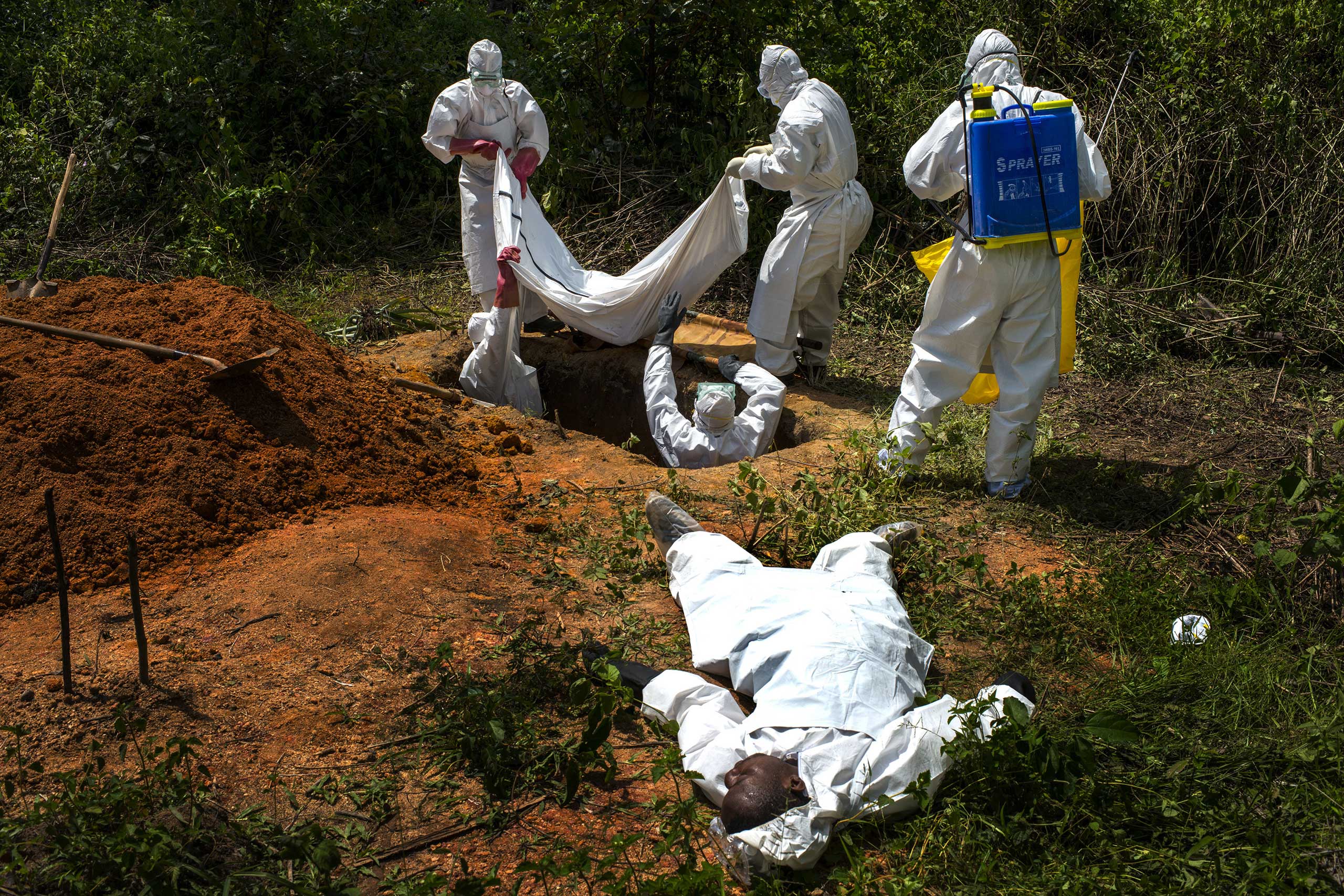Alexander Morris lays flat on his back after fainted due to the extreme heat inside a  protective suit while the Lofa County health department team buried his sister, on Nov. 7, 2014 in Voinjama, Liberia. Days later the health department said an Ebola test on the body was negative.