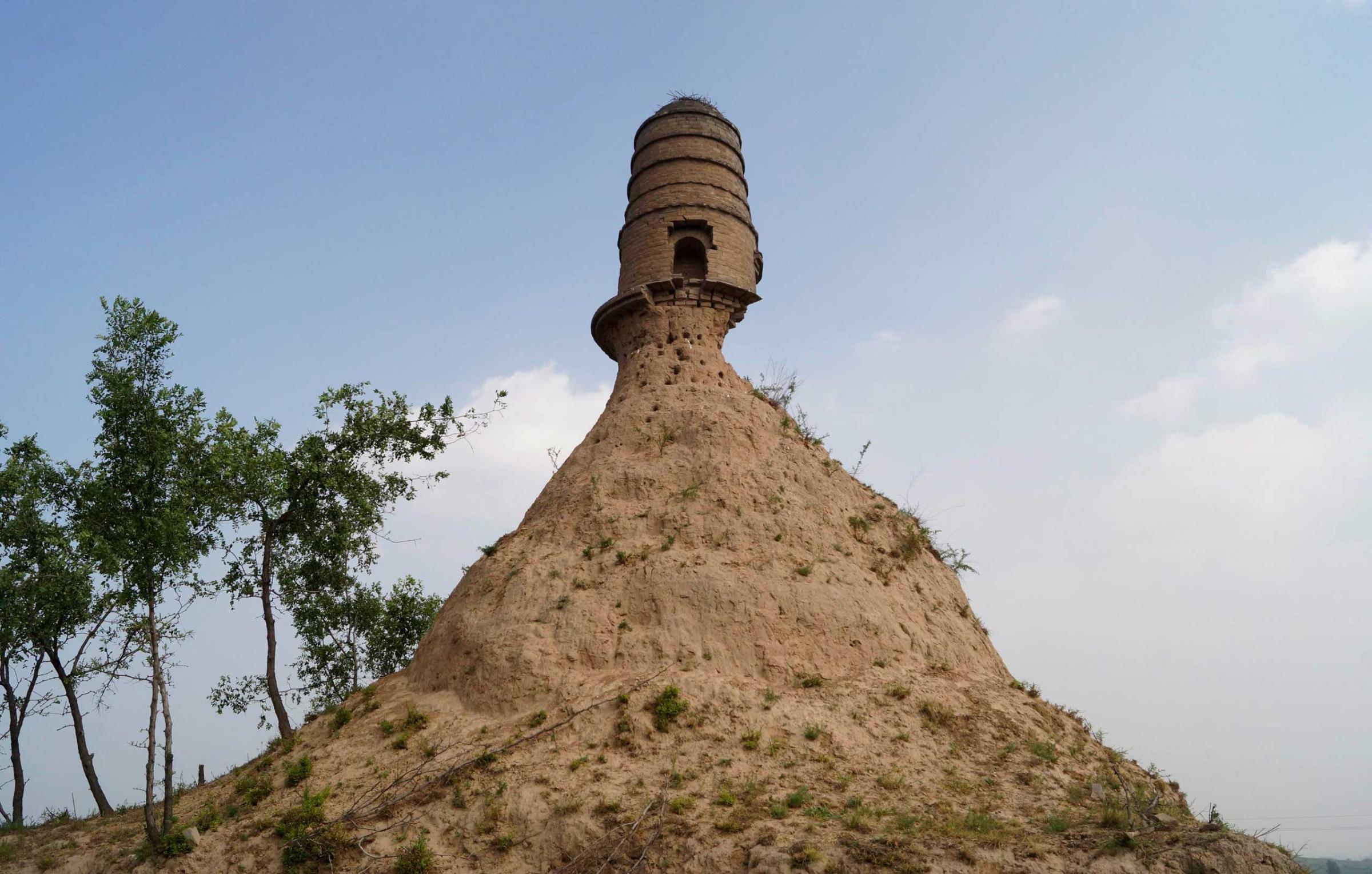 An ancient tower is seen balancing on the top of a dirt hill, with its base slightly eroded, along a grassland in Qixian county