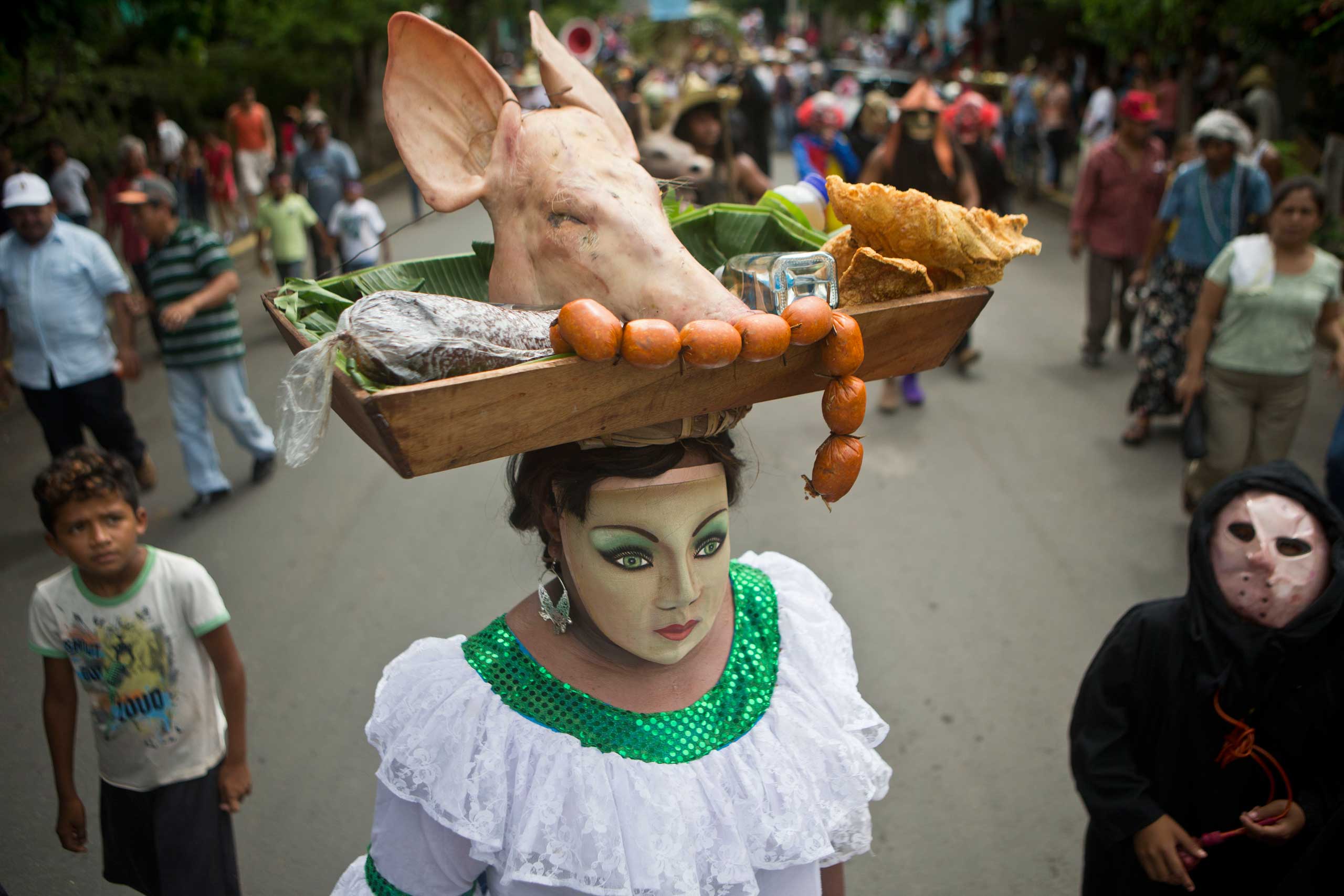 A man dressed as a woman carries a pig's head on a platter balanced on his head during the celebration of Torovenado, a satirical dance festival, in honor of Masaya's patron saint, San Jeronimo, in Masaya, Nicaragua, Oct 26, 2014.