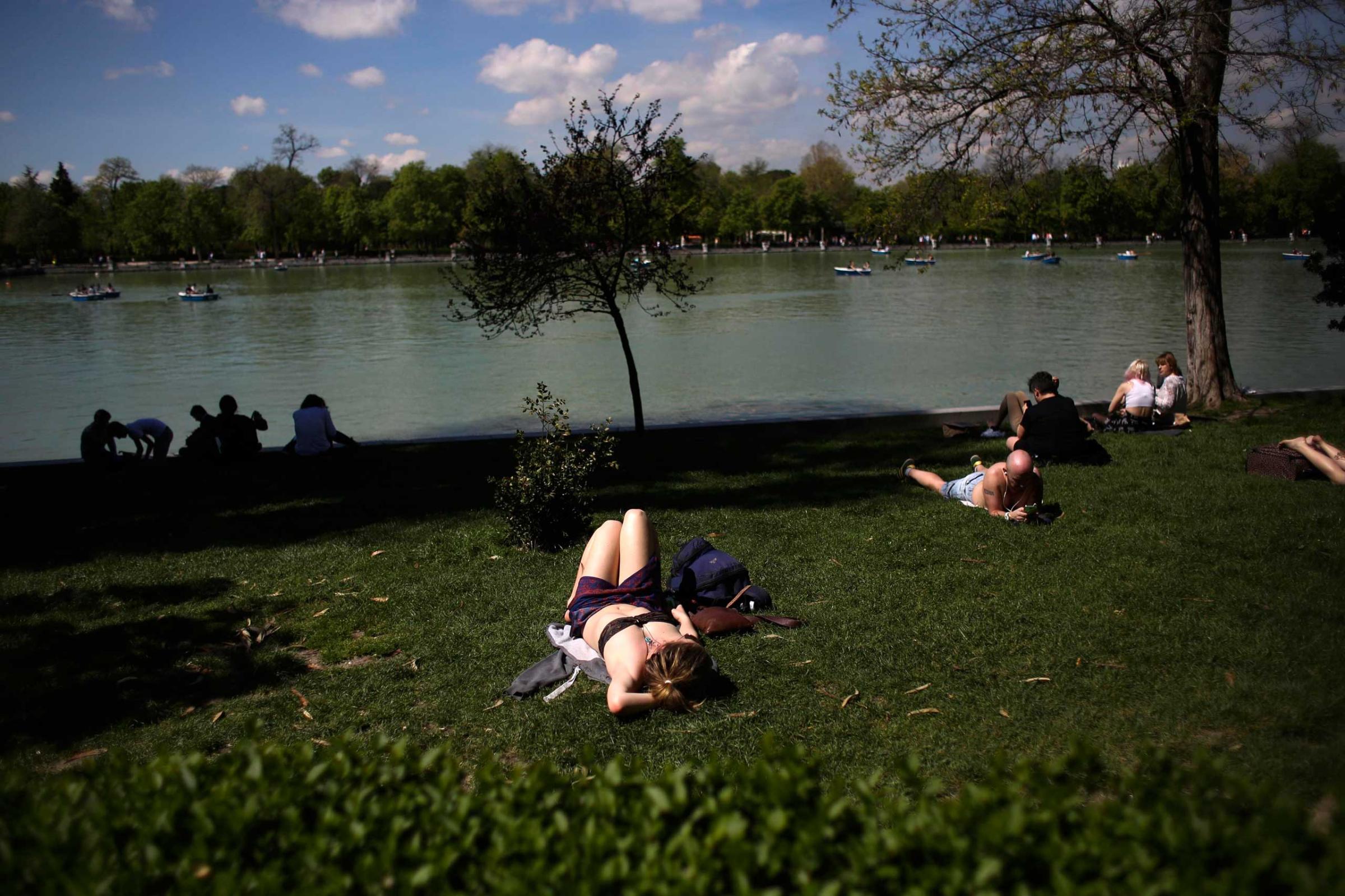 People sunbathe and watch boats on an artificial lake as they enjoy the warm weather during a sunny spring day at Madrid's Retiro park