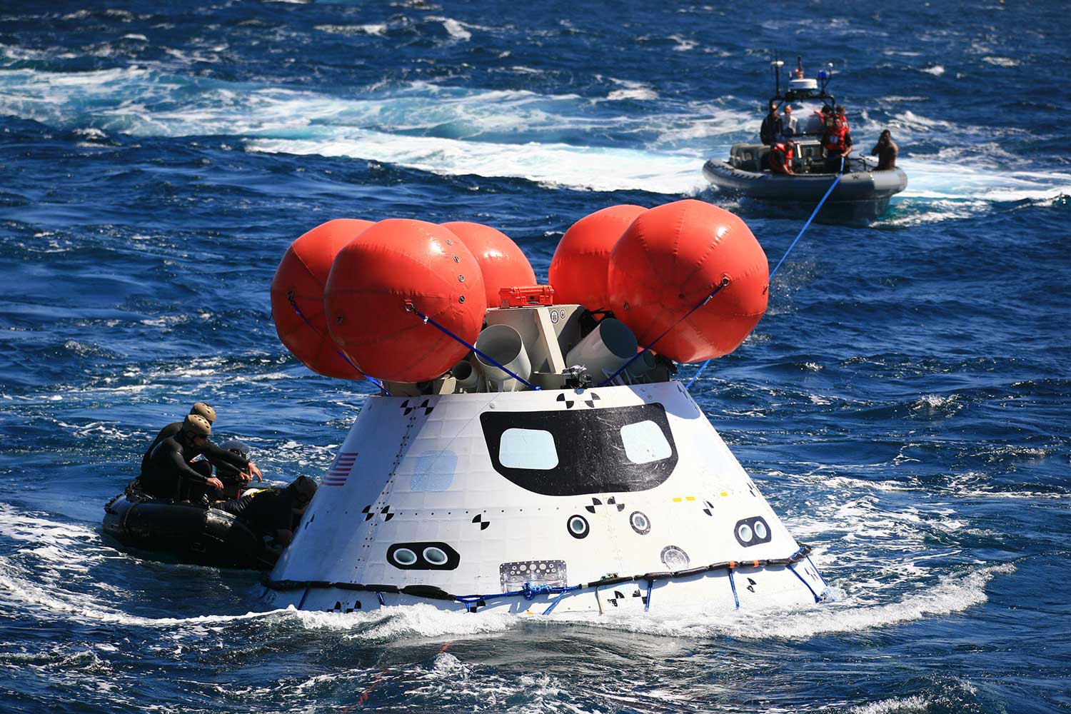 Team members work to secure a test version of Orion in the Pacific Ocean during a test recovery mission.