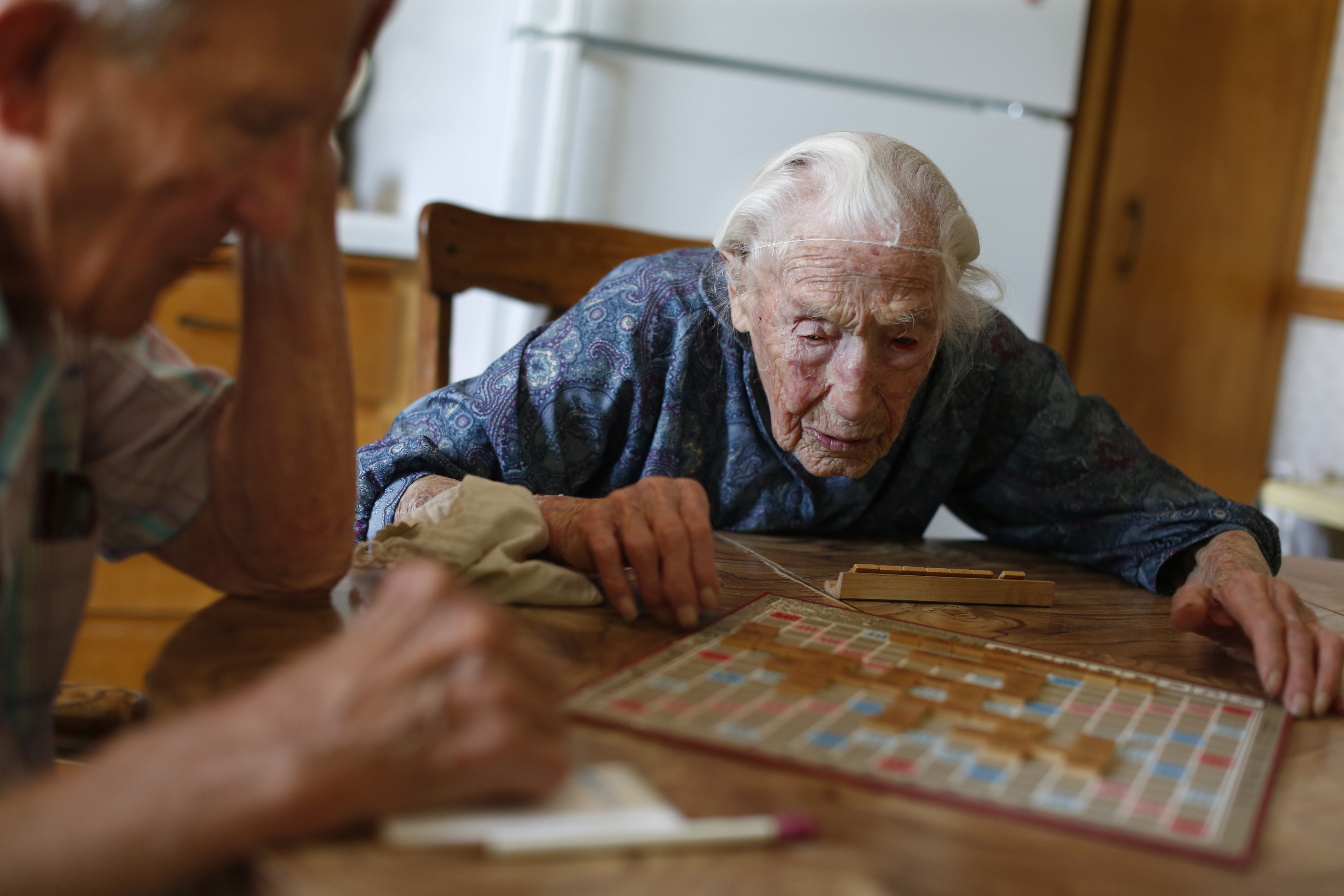 At her home in Pottsdam, Minn., Anna Stoehr plays Scrabble with her son Harlan, 83, who is changing the hoses on her washer (Richard Tsong-Taatarii&mdash;AP)