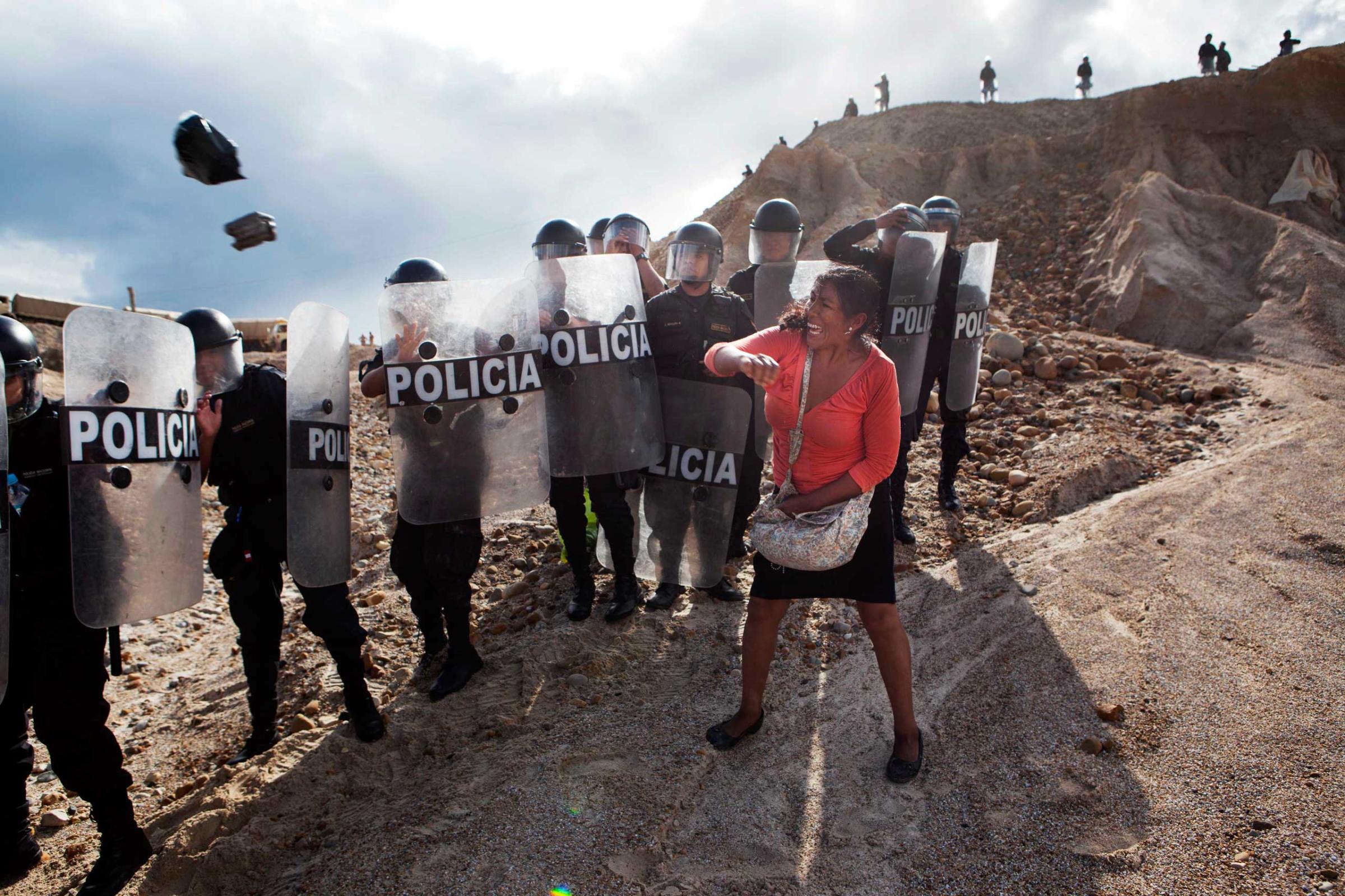 A woman throws a rock and a bag at police blocking her from getting home in the Huepetuhe district of the Madre de Dios region of Peru., April 28, 2014. Security forces began destroying illegal gold mining machinery in Peru’s southeastern jungle region of Madre de Dios, as authorities began enforcing a ban on illegal mining.