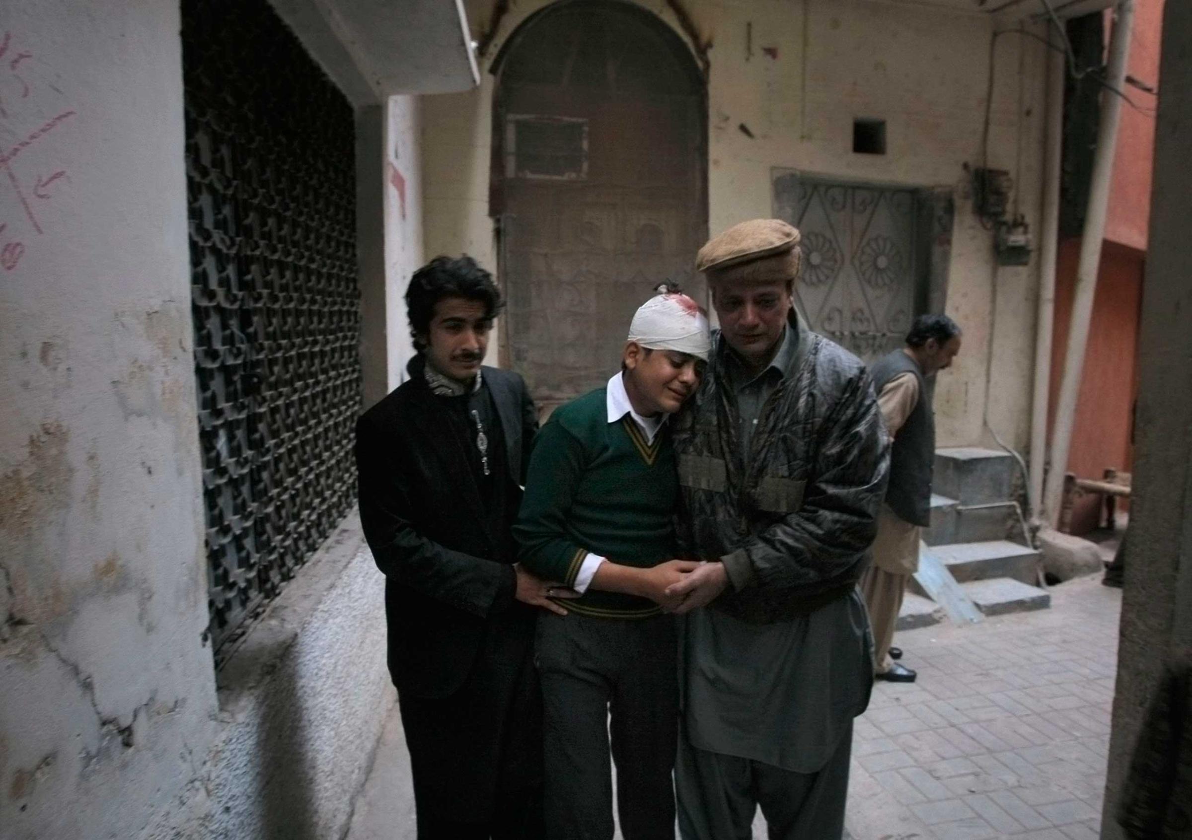The uncle and cousin of injured student Mohammad Baqair, center, comfort him as he mourns the death of his mother who was a teacher at the school which was attacked by Taliban, in Peshawar, Pakistan, Tuesday, Dec. 16, 2014.