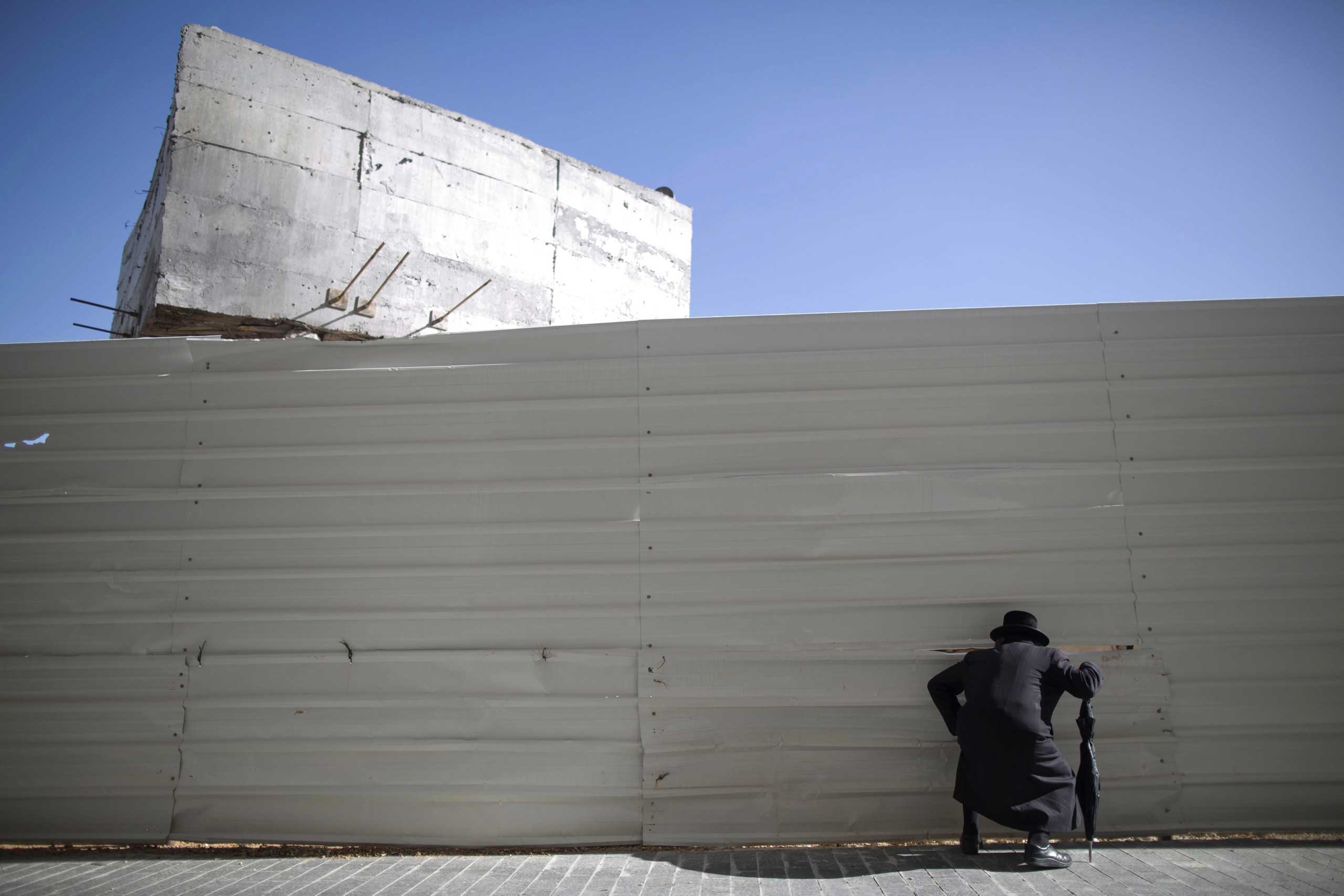 Dec. 10, 2014. An Ultra-Orthodox Jewish man peeks through fence around a new construction site in downtown Jerusalem.  Hundreds of Ultra-Orthodox Jews protested against the construction of new housing units, believing that they would be built at the site of ancient Jewish graves.