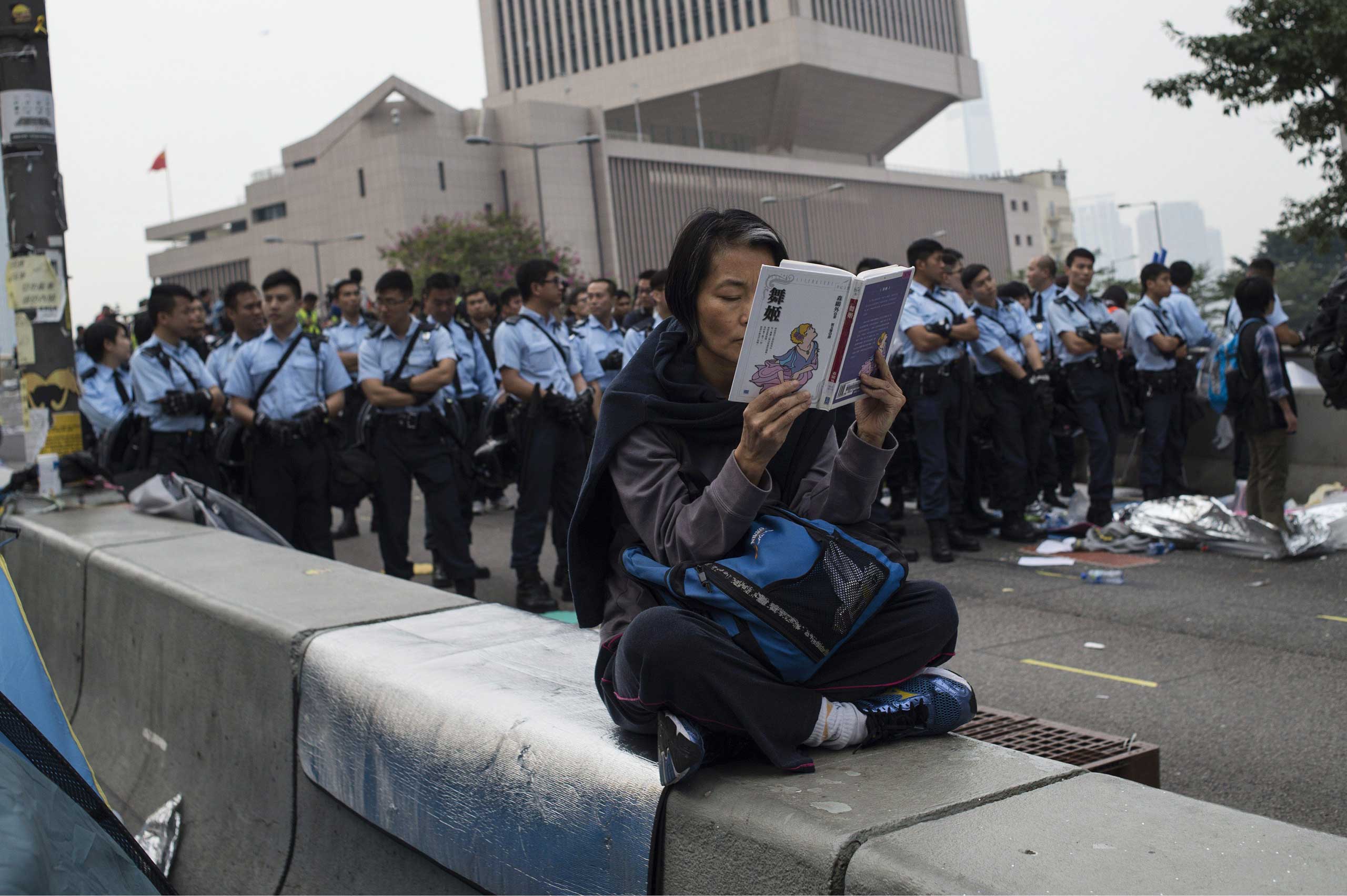 Dec. 11, 2014. A woman reads a book at the side of the road as Hong Kong police stand guard during the dismantling of the main pro-democracy protest camp in Hong Kong.