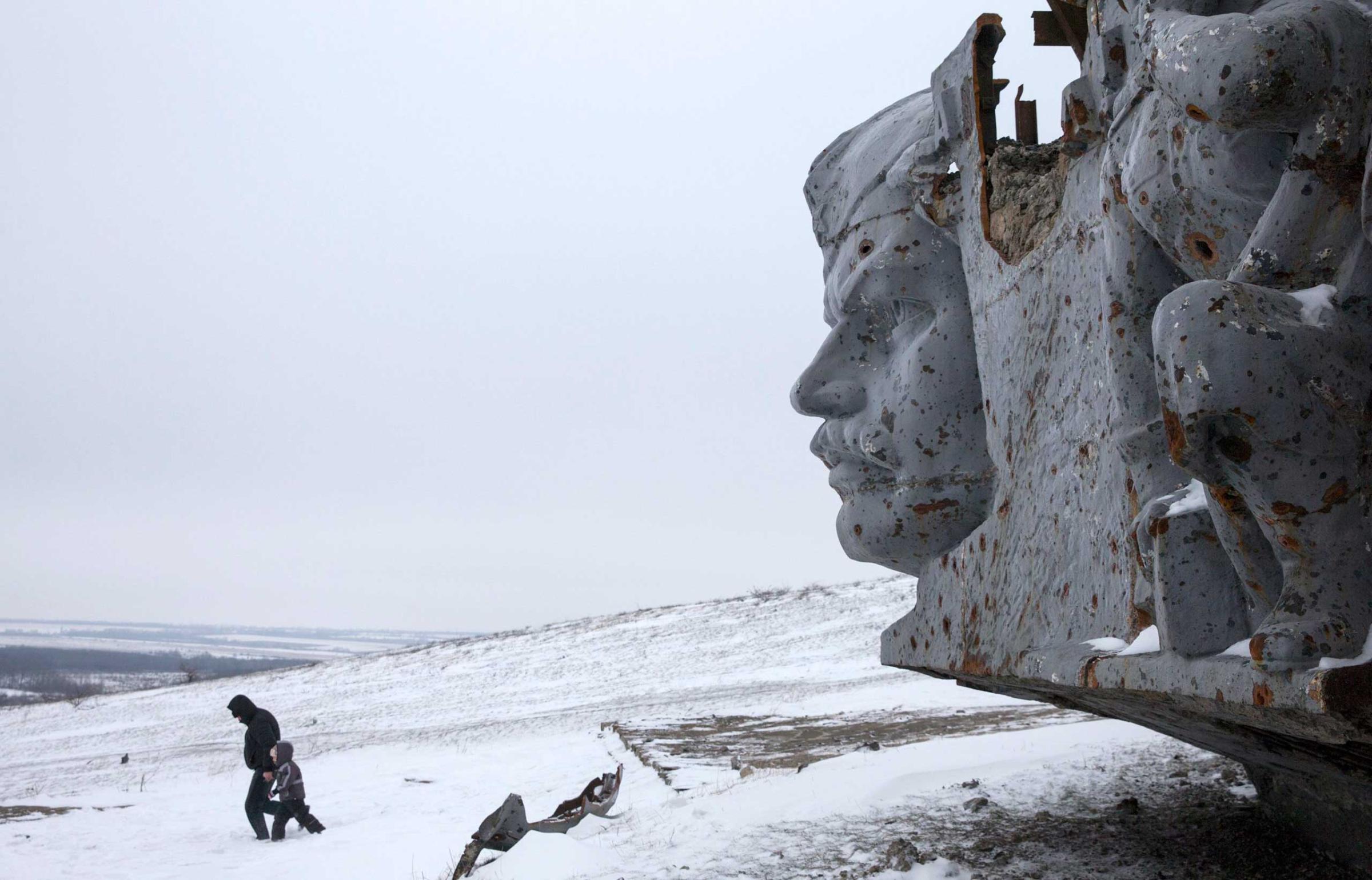 A man and a child walk in the snow at the destroyed war memorial at Savur-Mohyla, a hill east of the city of Donetsk
