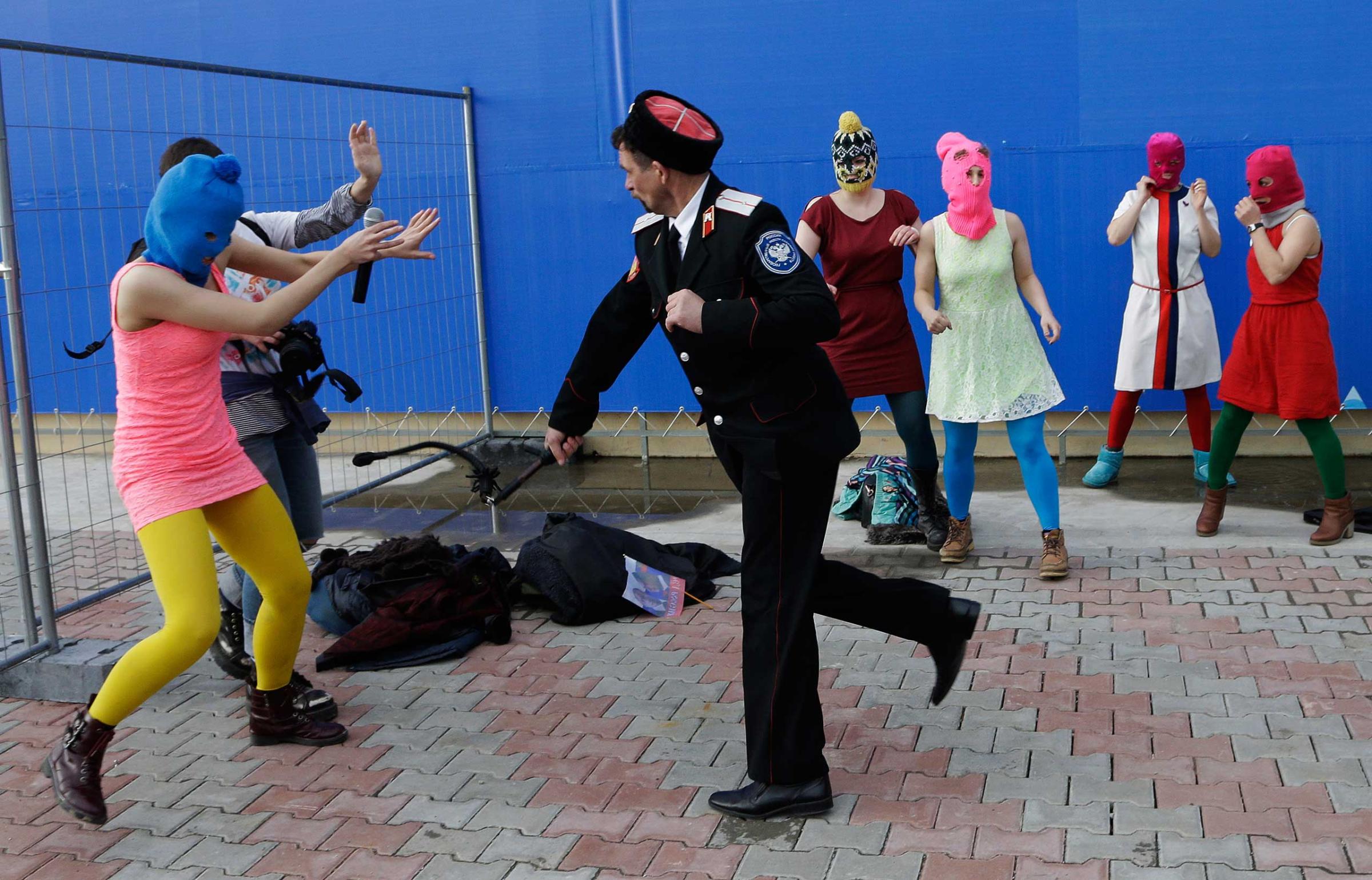 A Cossack militiaman attacks Nadezhda Tolokonnikova and a photographer as she and fellow members of the punk group Pussy Riot, including Maria Alekhina, center, in the pink balaclava, stage a protest performance in Sochi, Russia, Feb. 19, 2014.